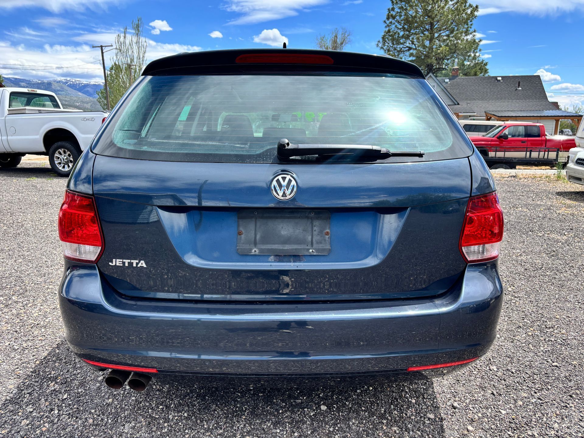 Rear view of a blue Volkswagen hatchback parked on a gravel lot under a partly cloudy sky