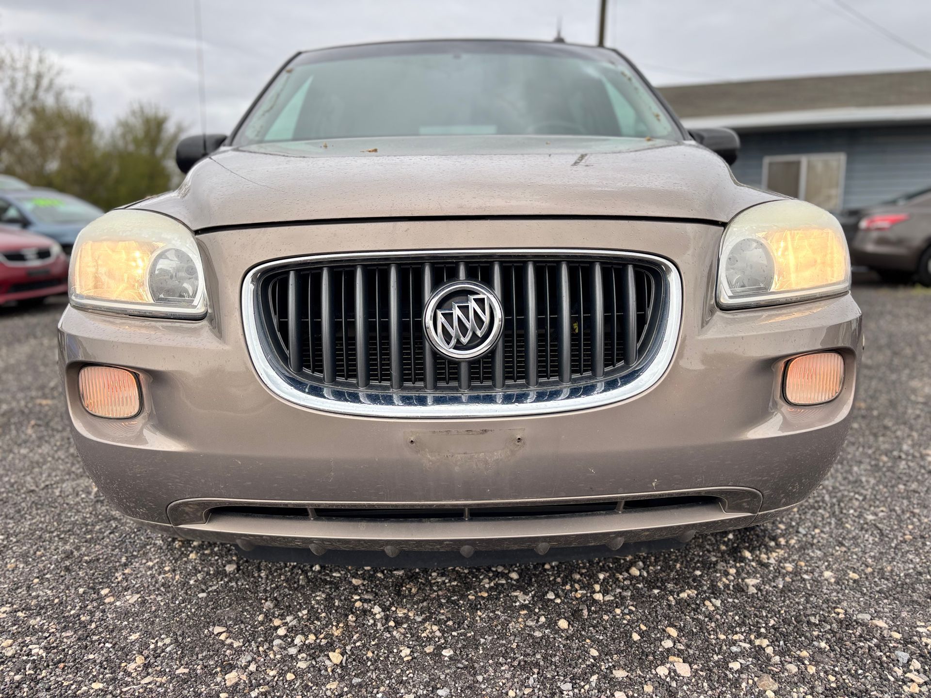 Front view of a dusty Buick SUV with headlights on, parked outdoors on gravel.