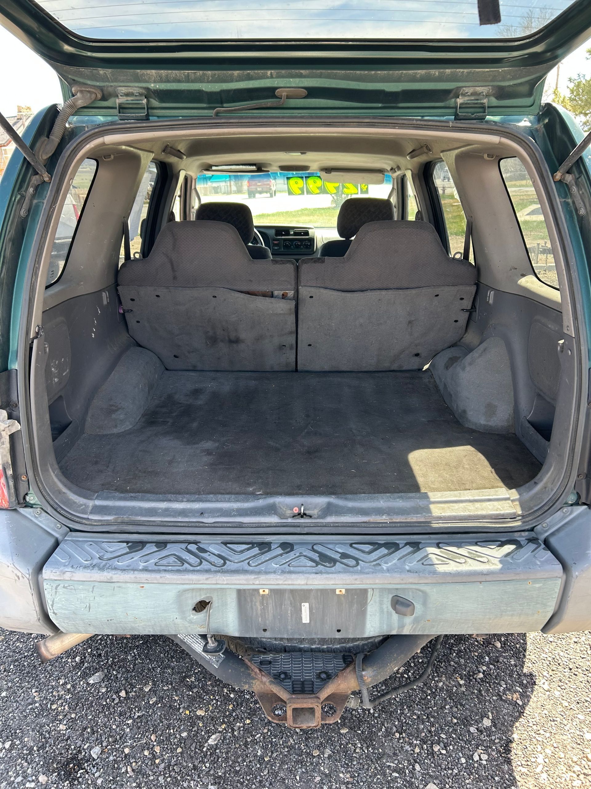 Open SUV cargo area with rear seats folded down, showing a dirty gray trunk and tow hitch.