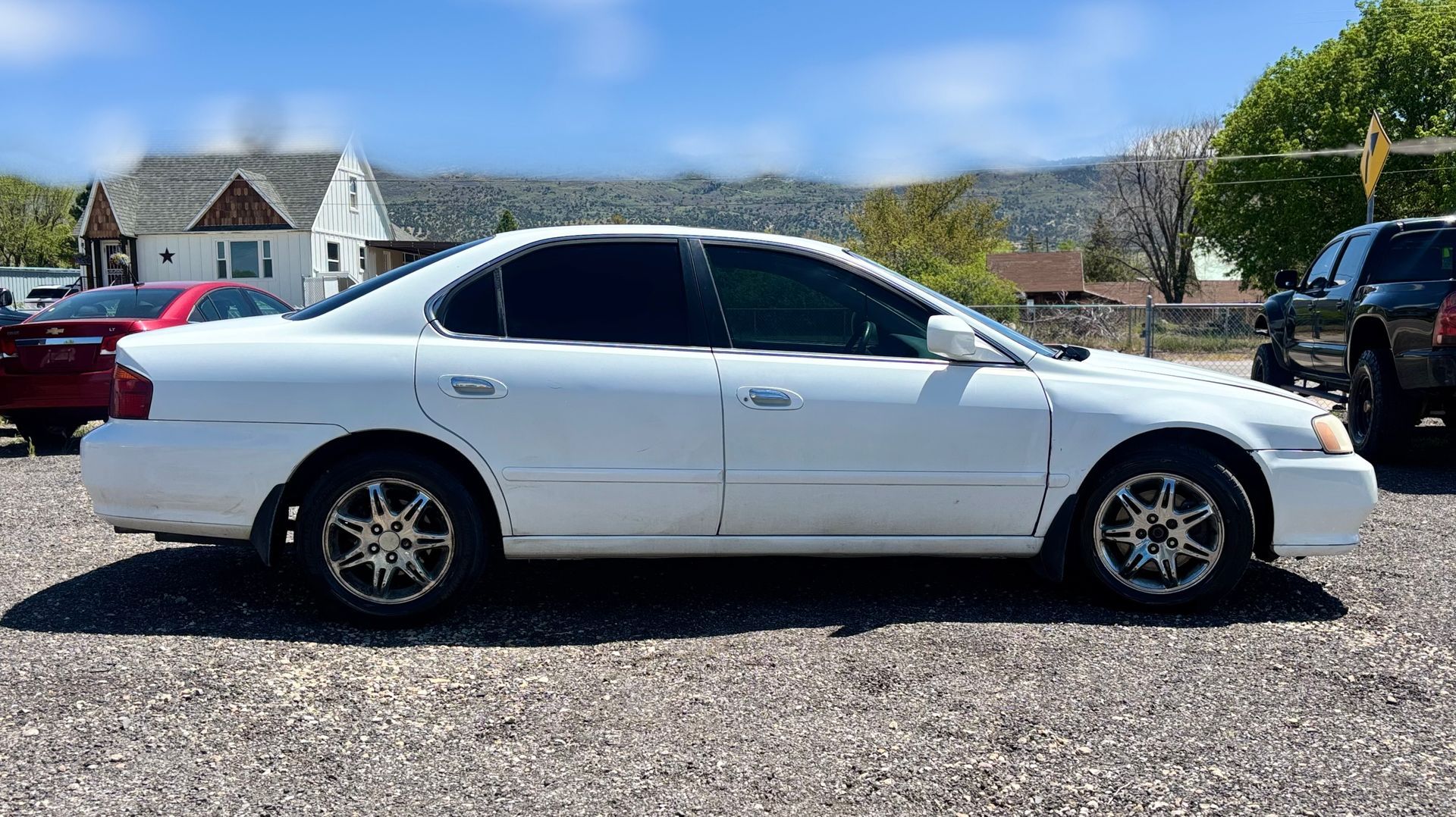 White sedan parked on a gravel lot under a blue sky, side view