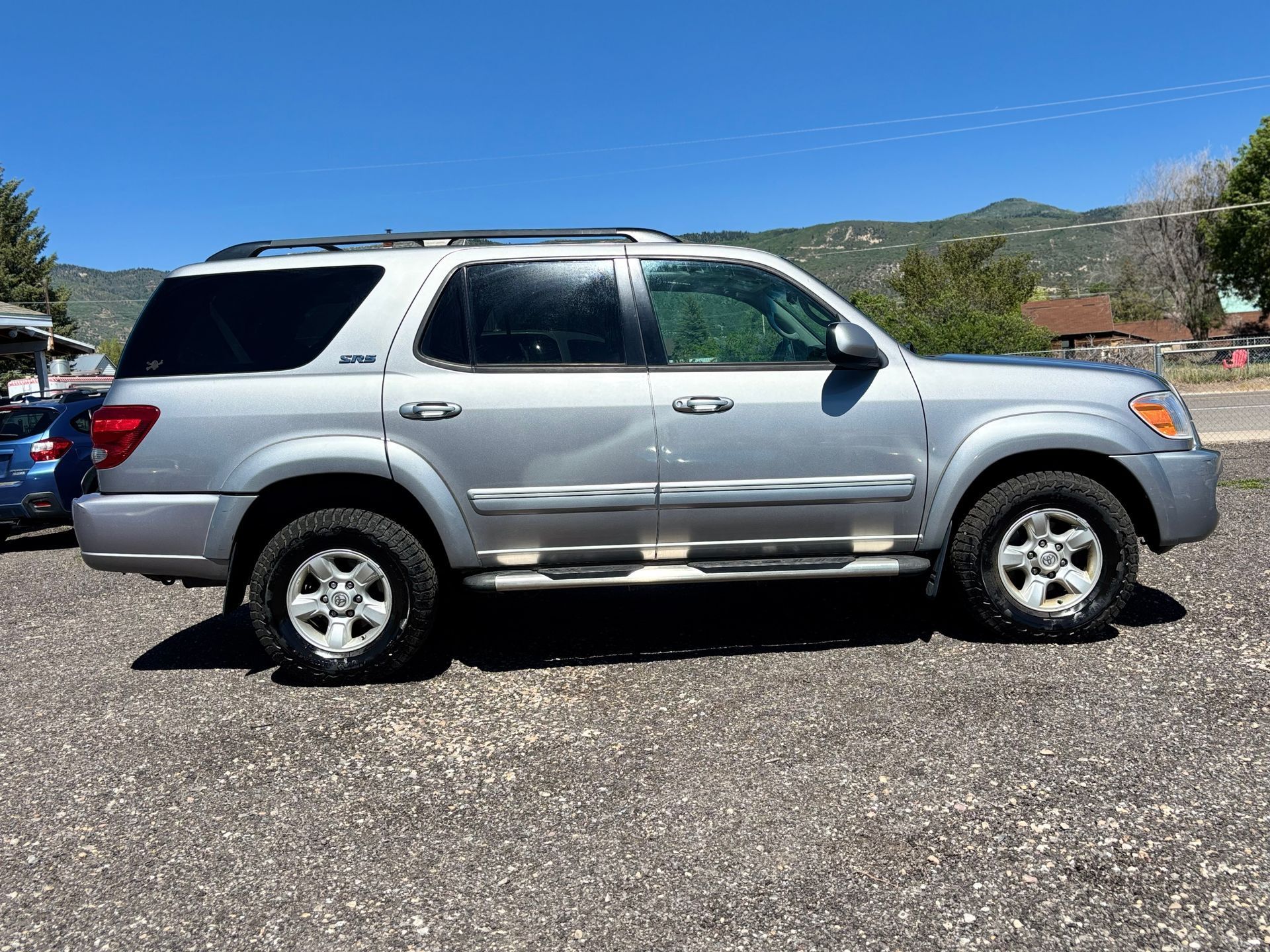 Silver SUV parked on a gravel lot under a clear blue sky, with mountains in the background