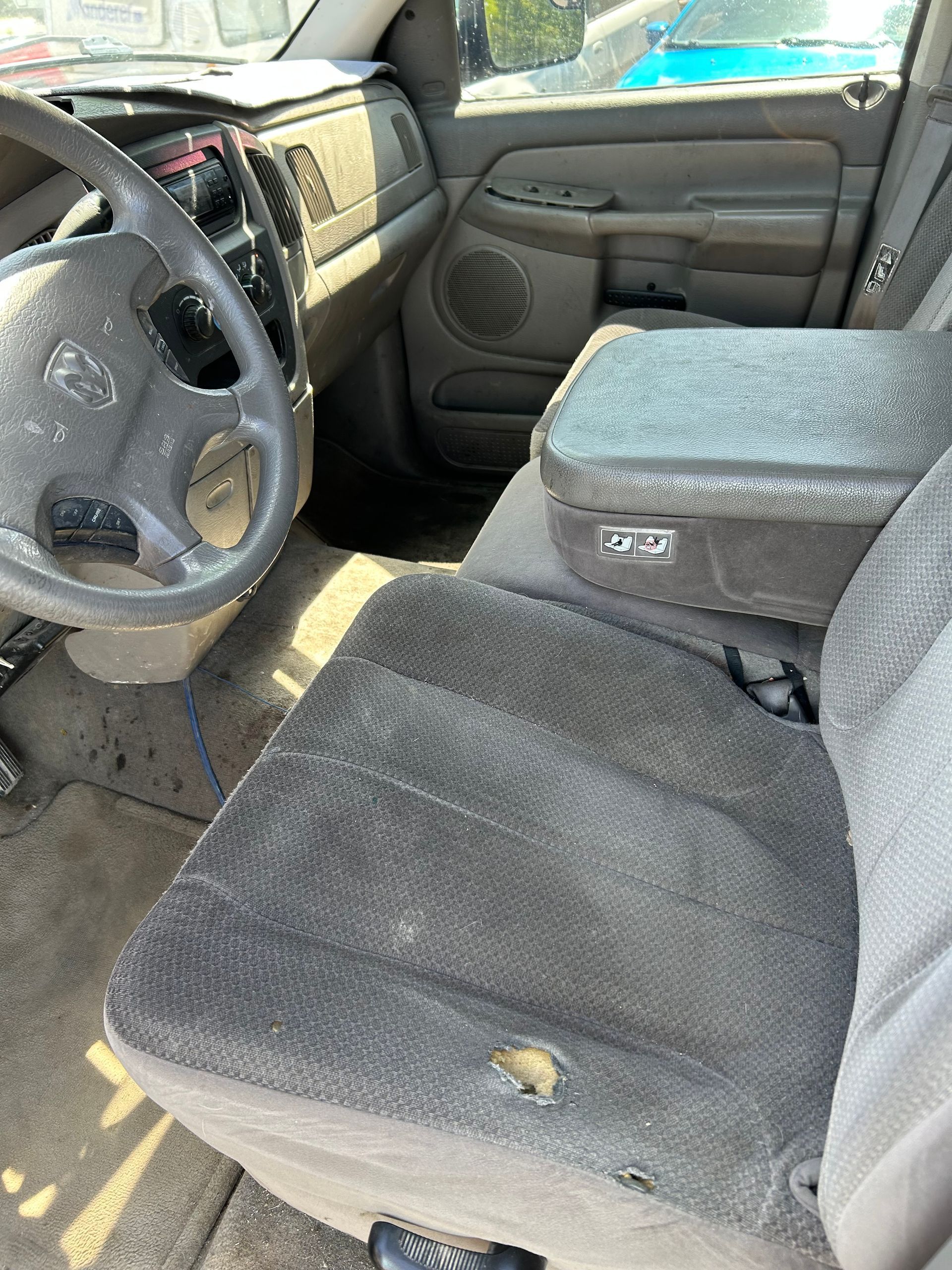 Car interior with worn gray cloth seats, steering wheel, and dusty dashboard area