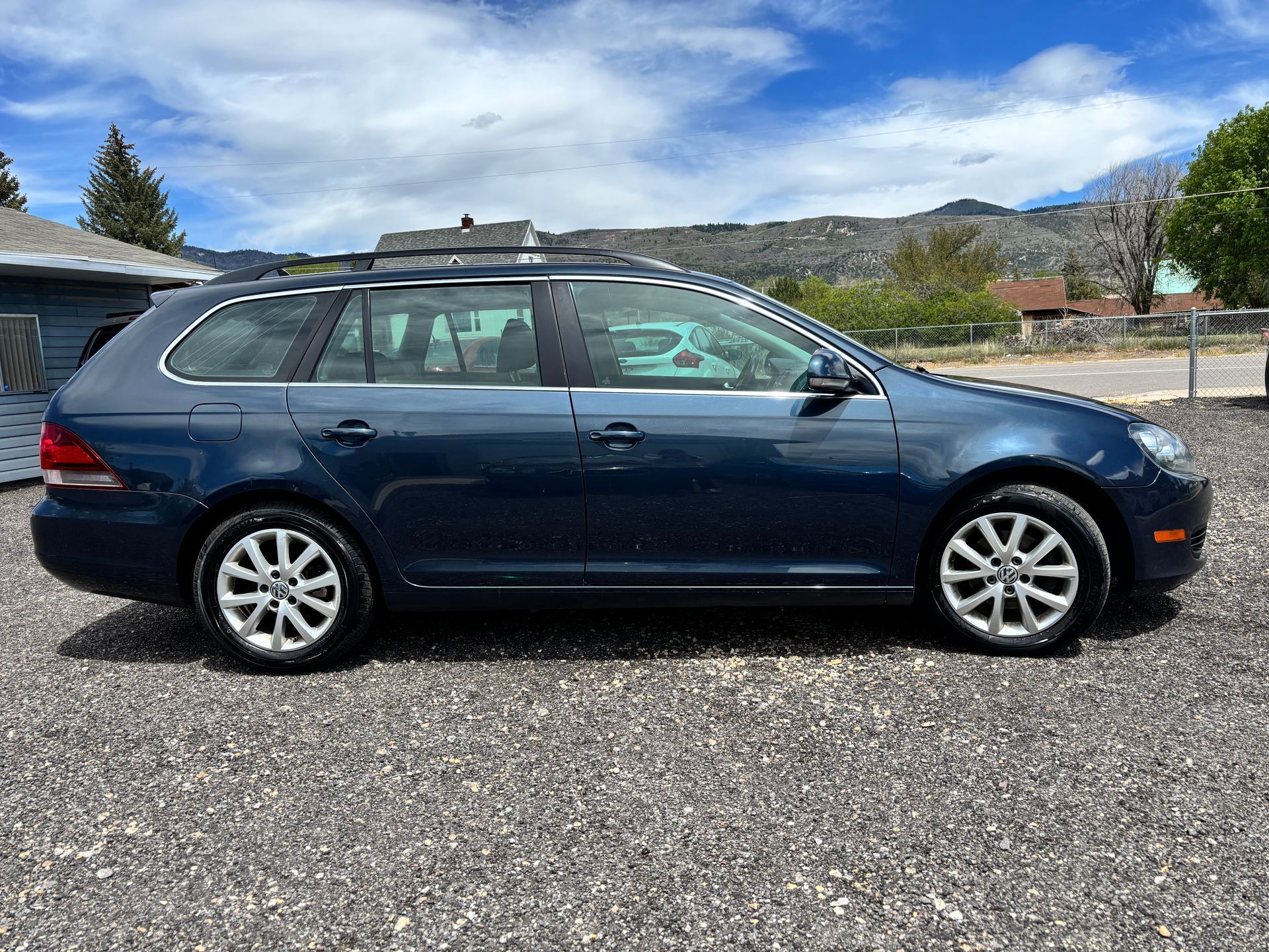 Dark blue station wagon parked on gravel with mountains and blue sky in the background