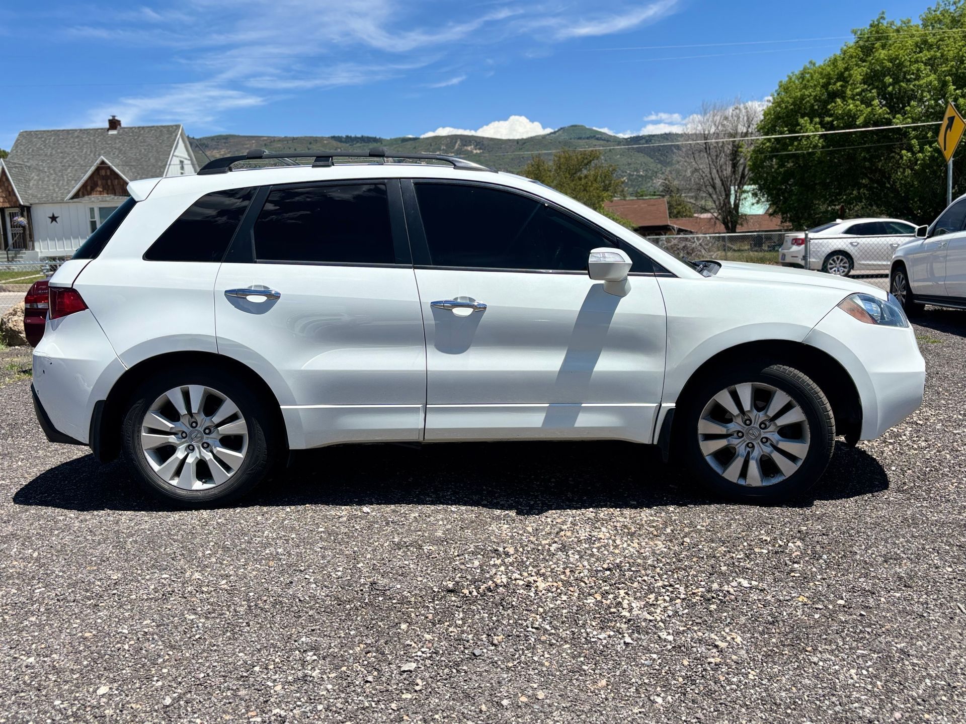 White SUV parked on a gravel lot with mountains and houses in the background