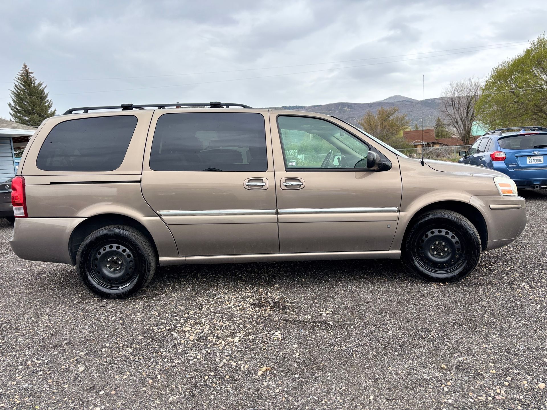 Tan minivan parked on gravel lot under cloudy sky, with dark tinted windows and black wheels