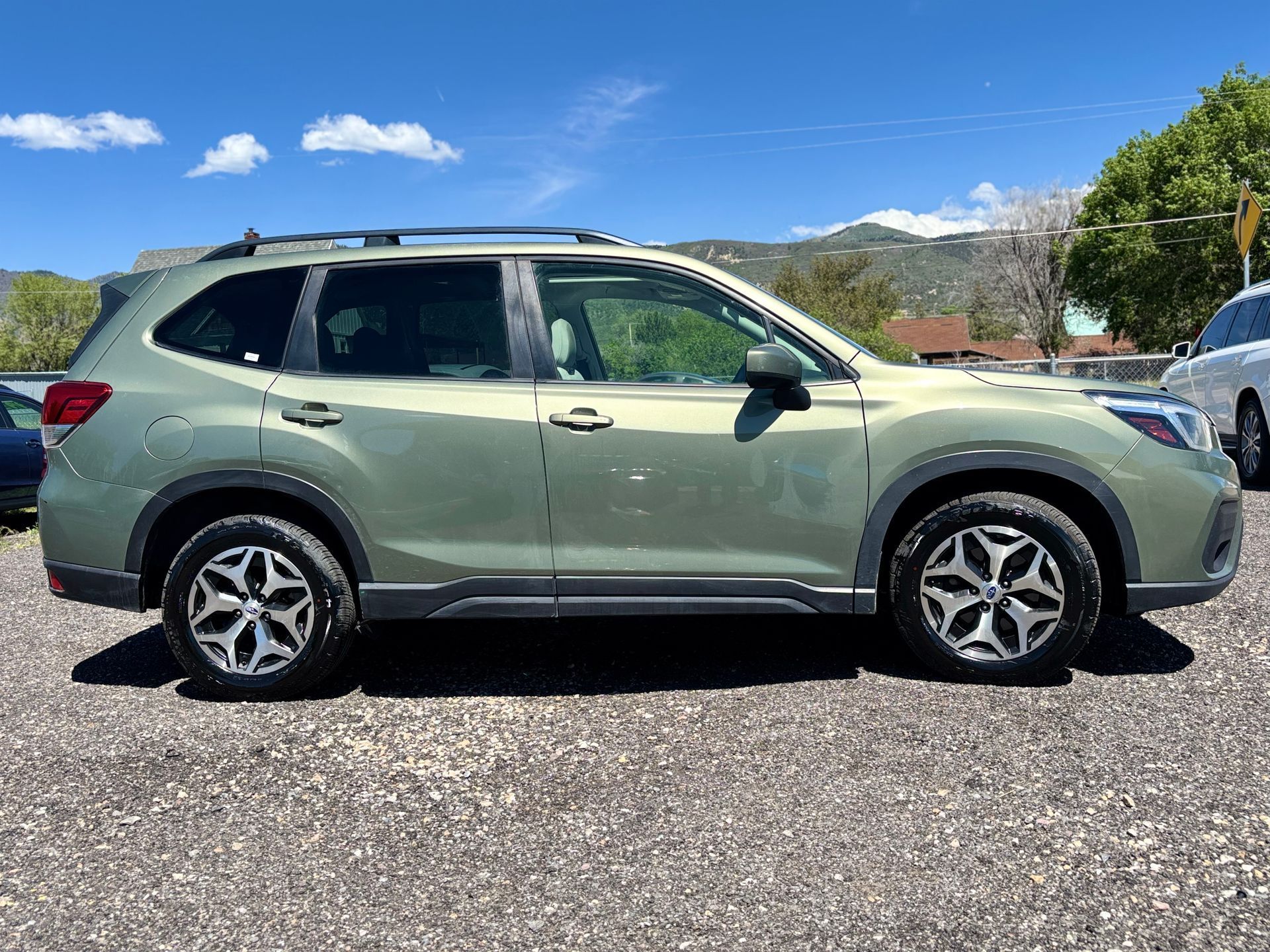 Green SUV parked on gravel under a blue sky with mountains in the background