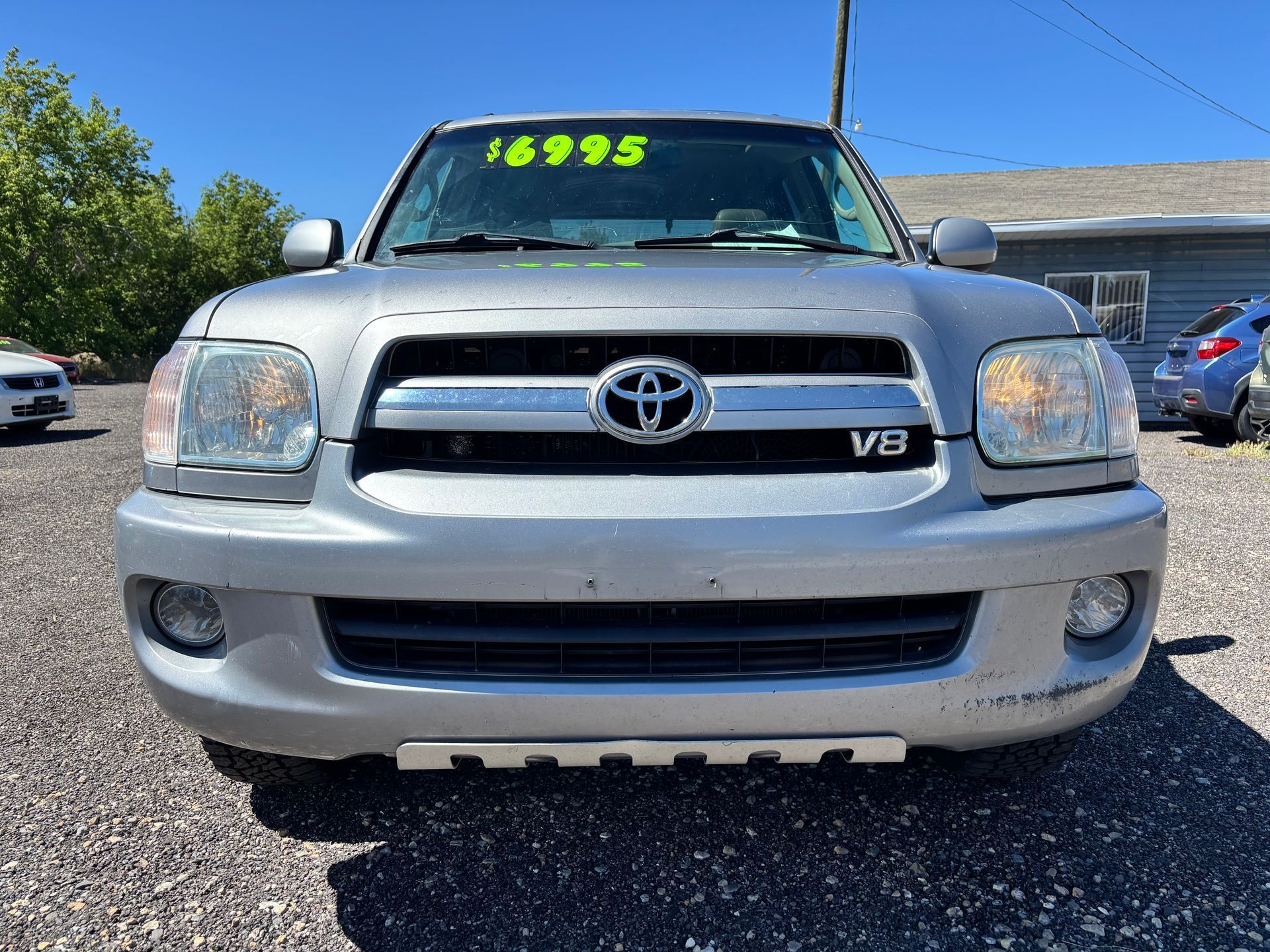 Front view of a silver Toyota truck with a V8 badge, parked outdoors under bright sun.