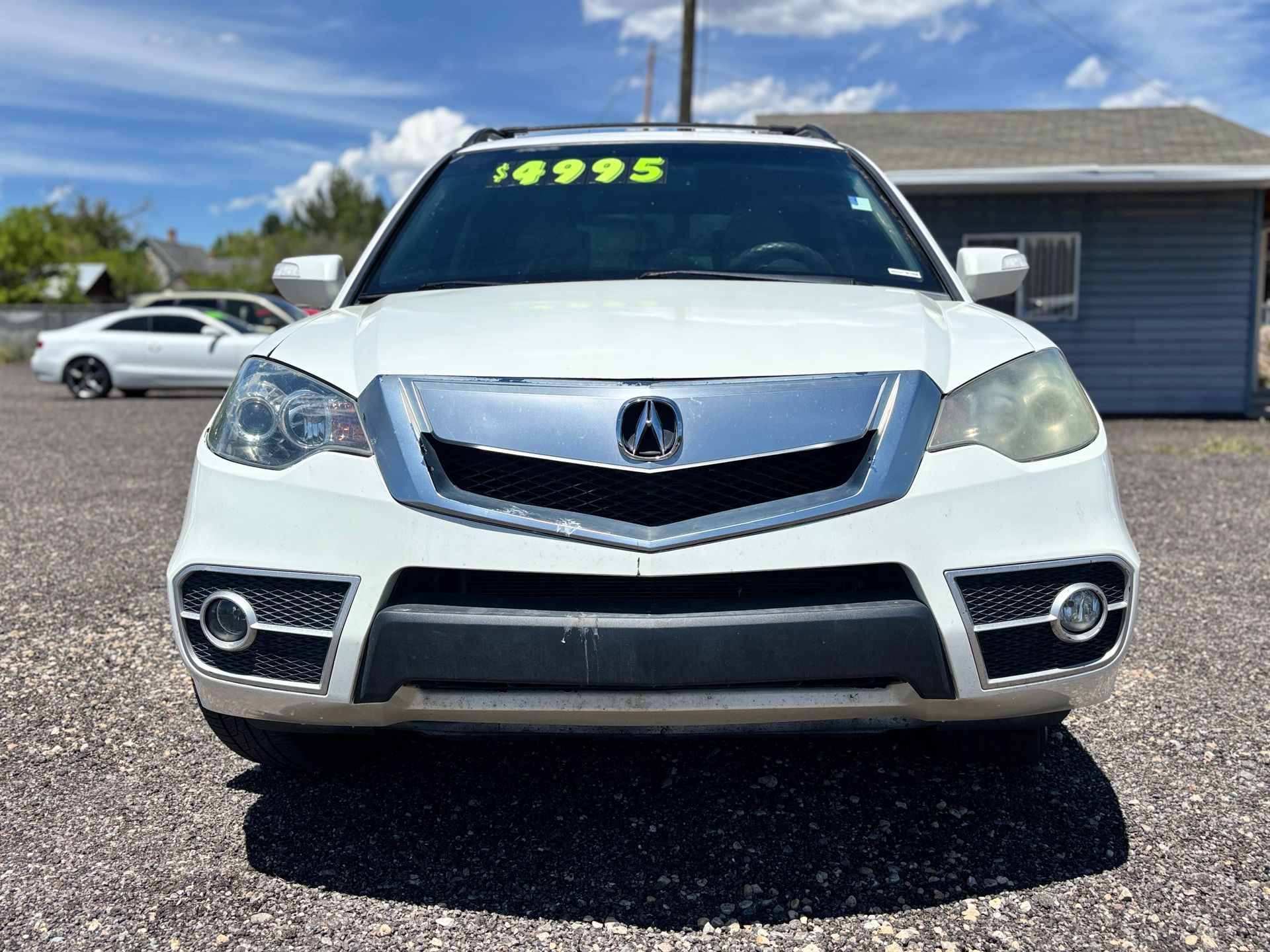 Front view of a white Acura SUV with price stickers, parked on a sunny lot.