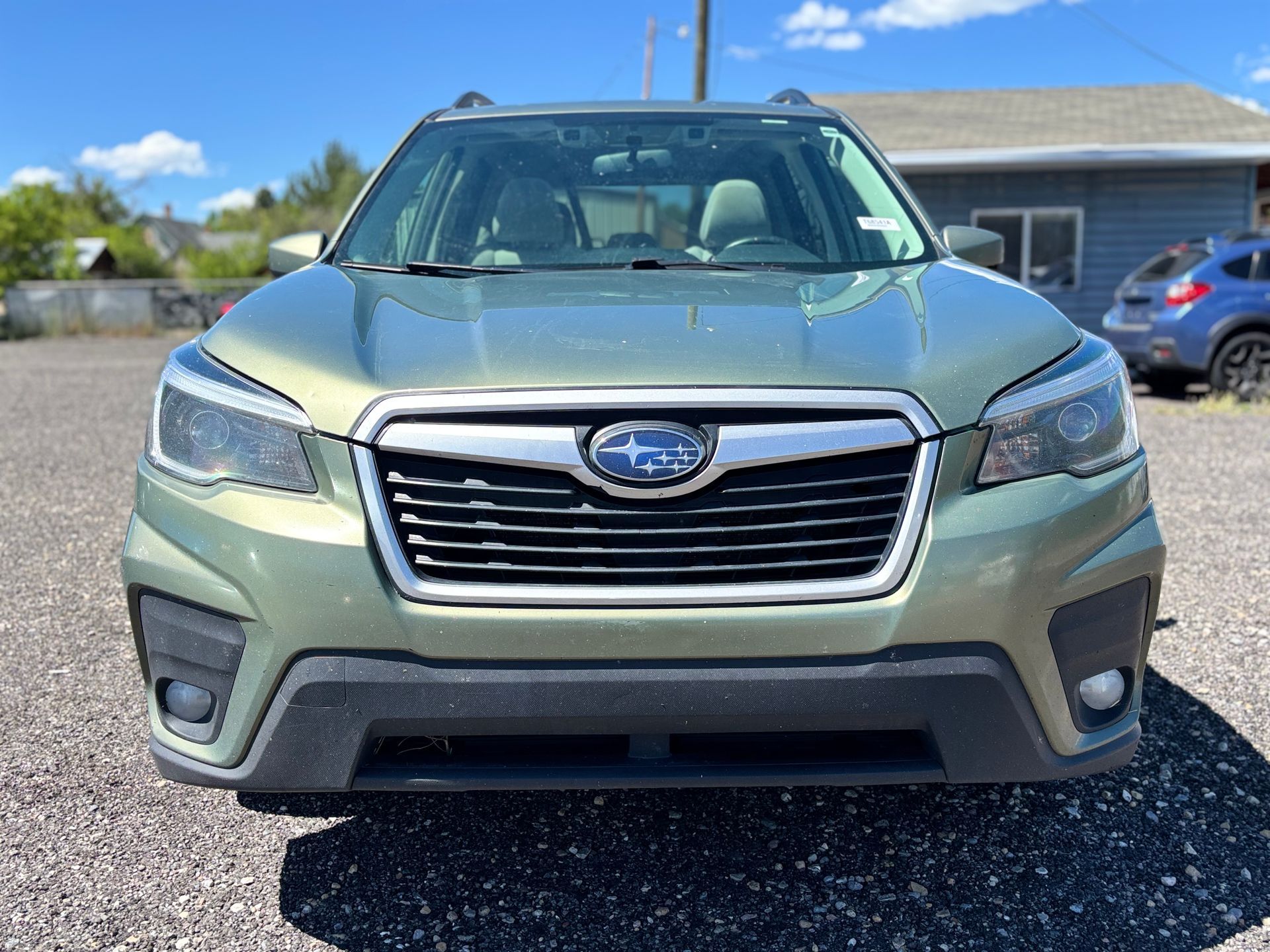 Front view of a green Subaru SUV parked on a sunny street near houses