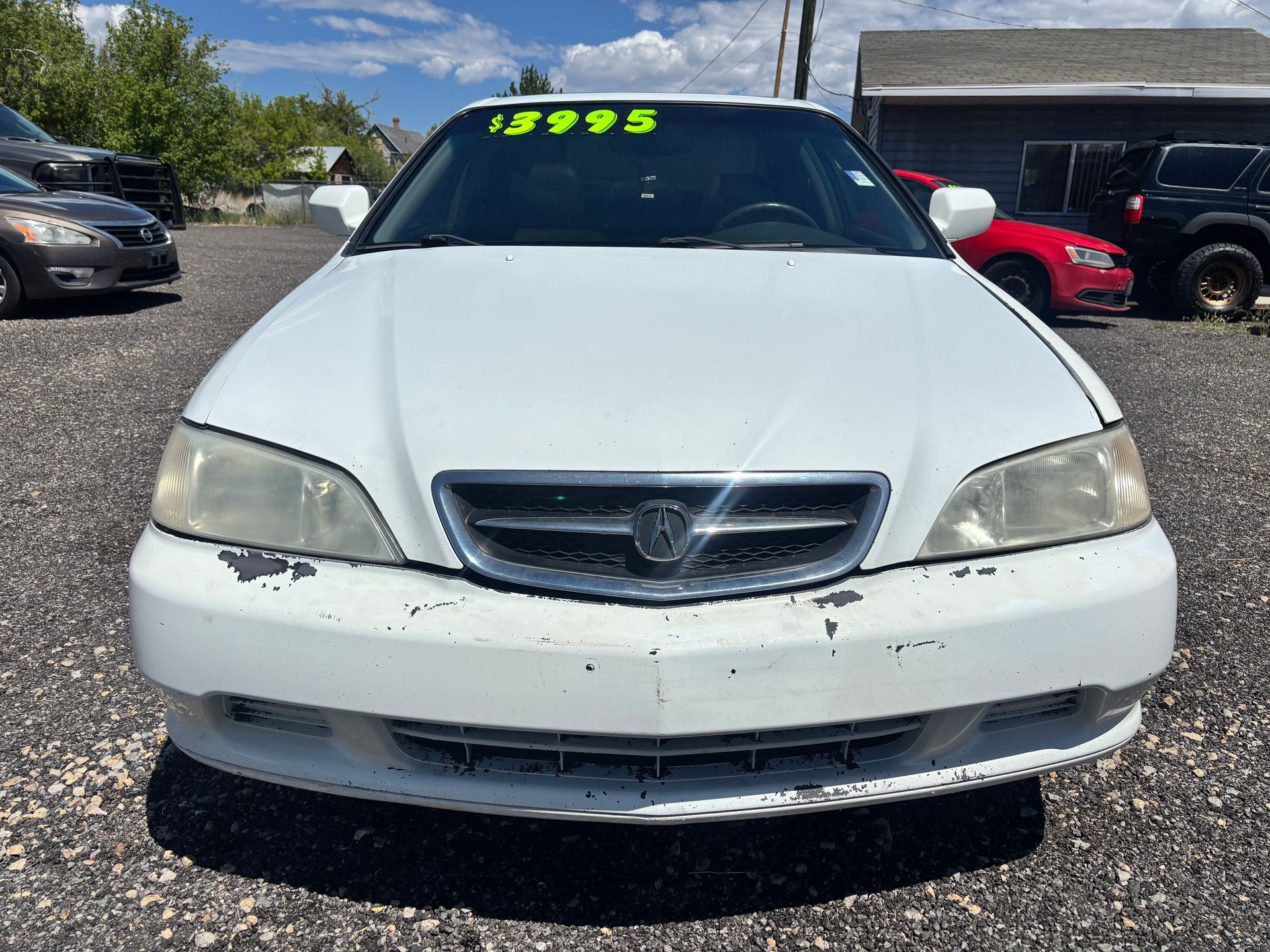 Front view of a white sedan with a green price tag on the windshield in a parking lot