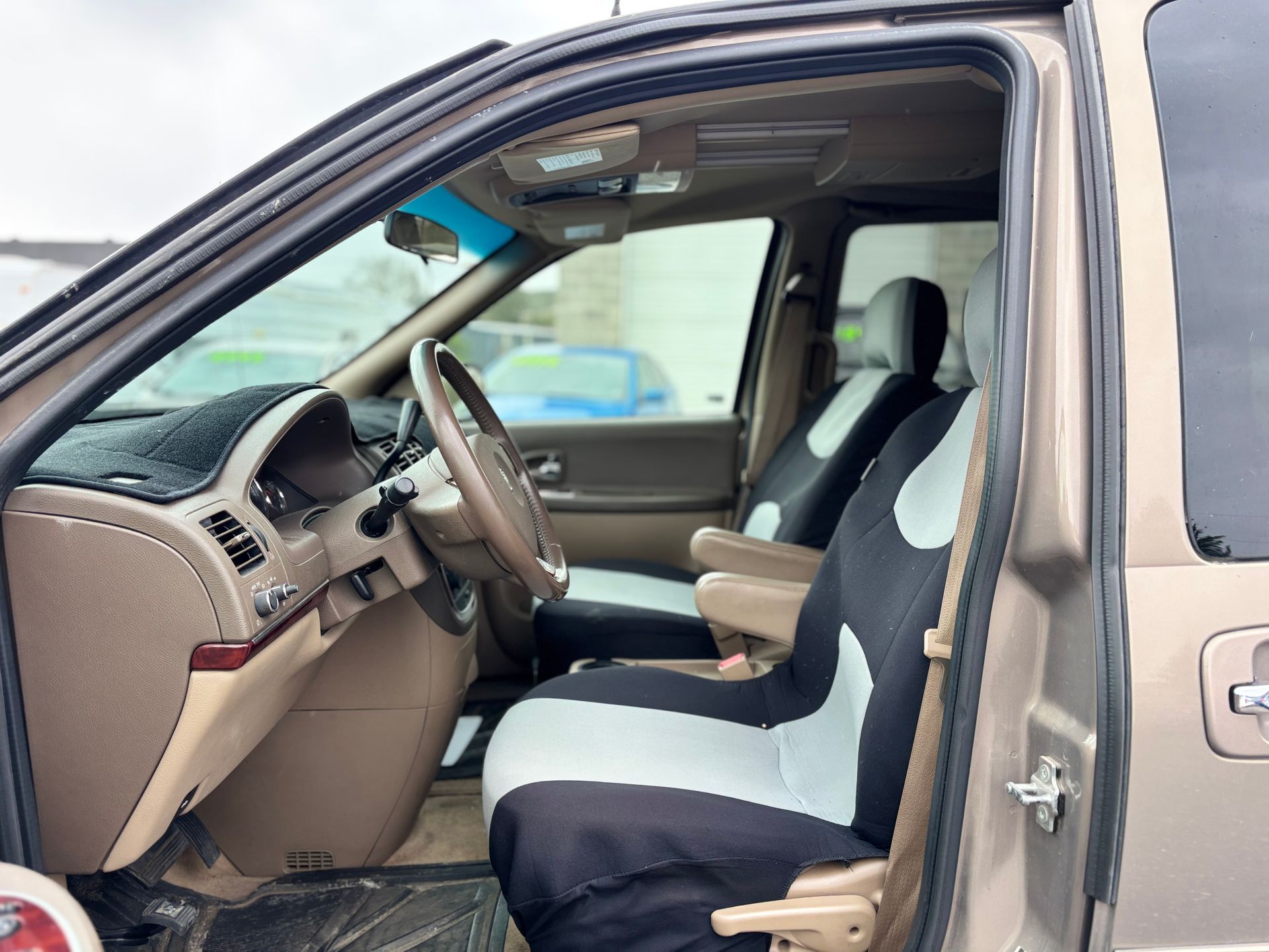Open car door showing beige interior with front seats and steering wheel.