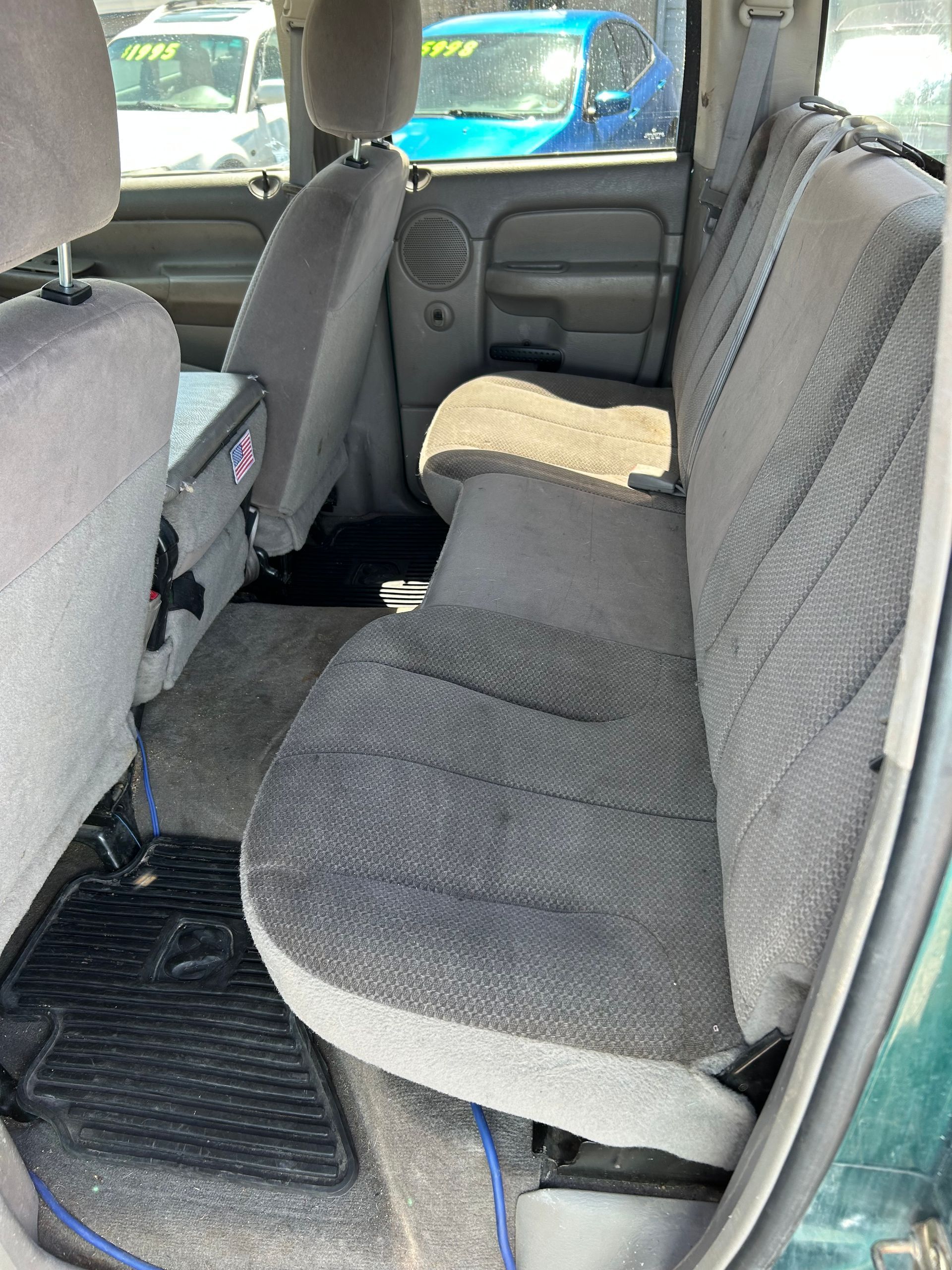 Rear seat of a vehicle with gray fabric bench seats and black floor mats, viewed from the open side door