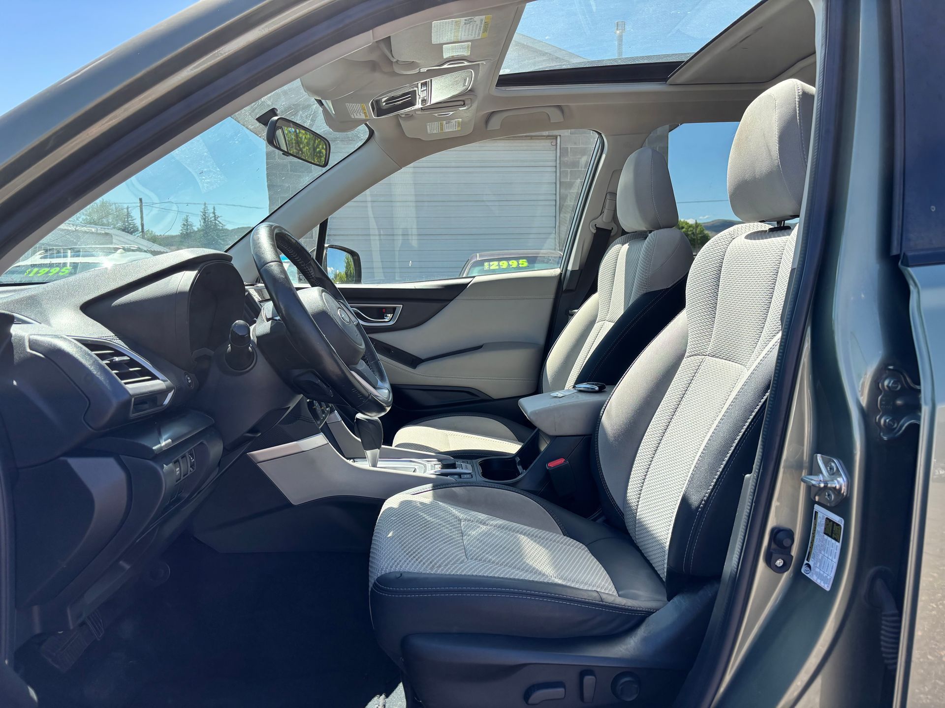 Car interior with open front door, gray seats, and a sunroof in daylight