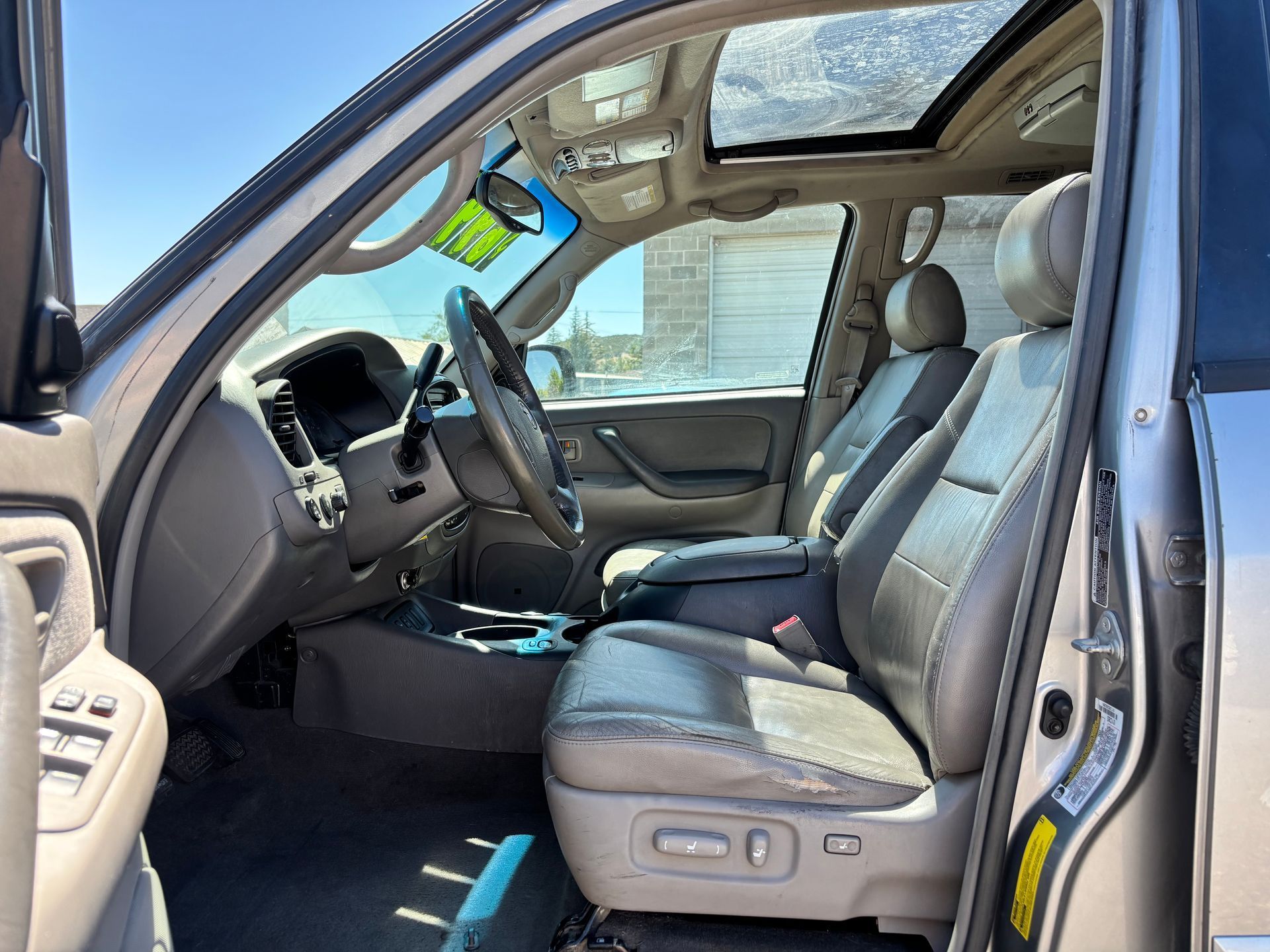 Car interior with front passenger door open, showing gray leather seats and sunroof in daylight