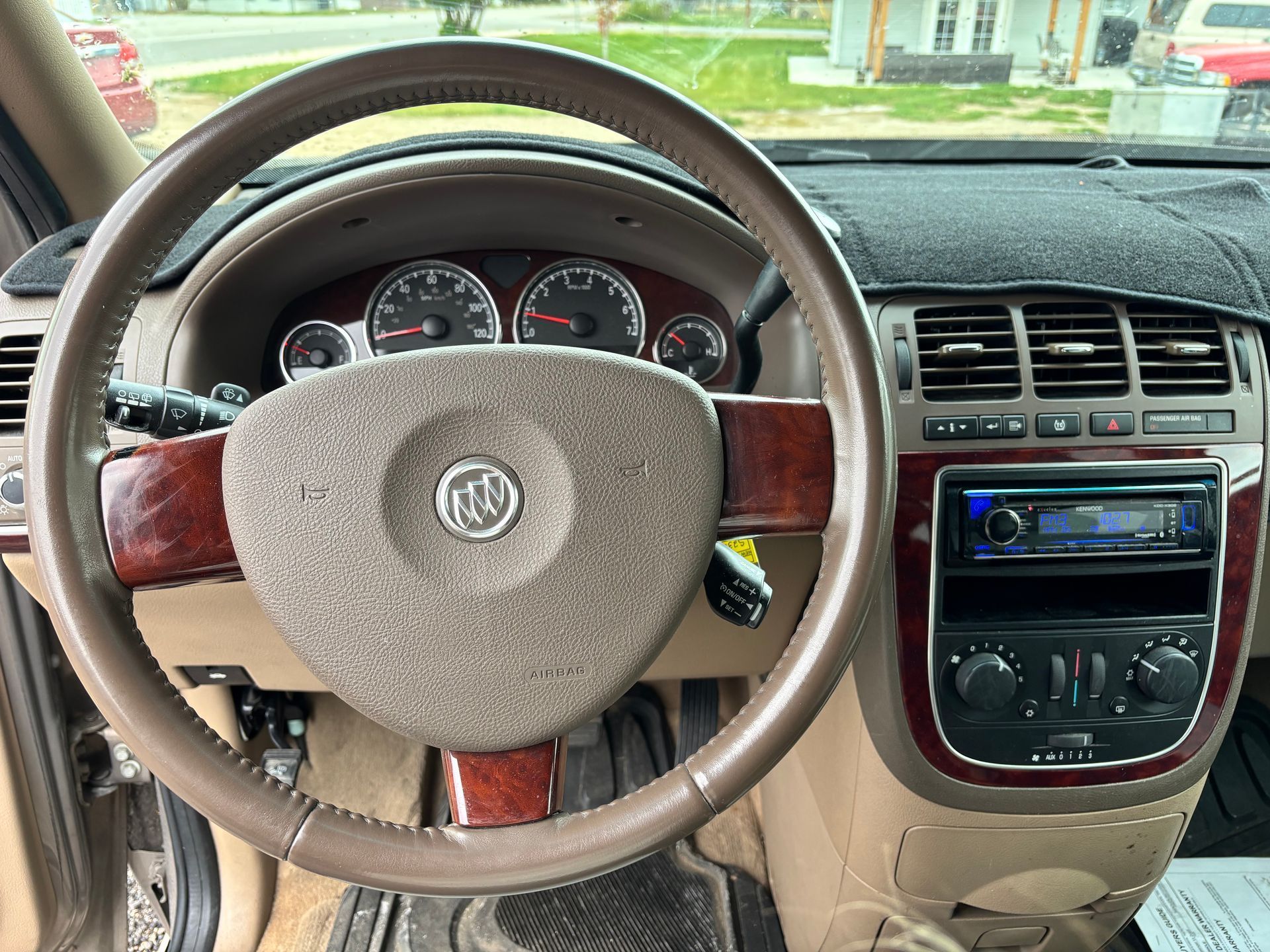 Car interior view of a tan dashboard with wood-trim steering wheel, gauges, and center console.