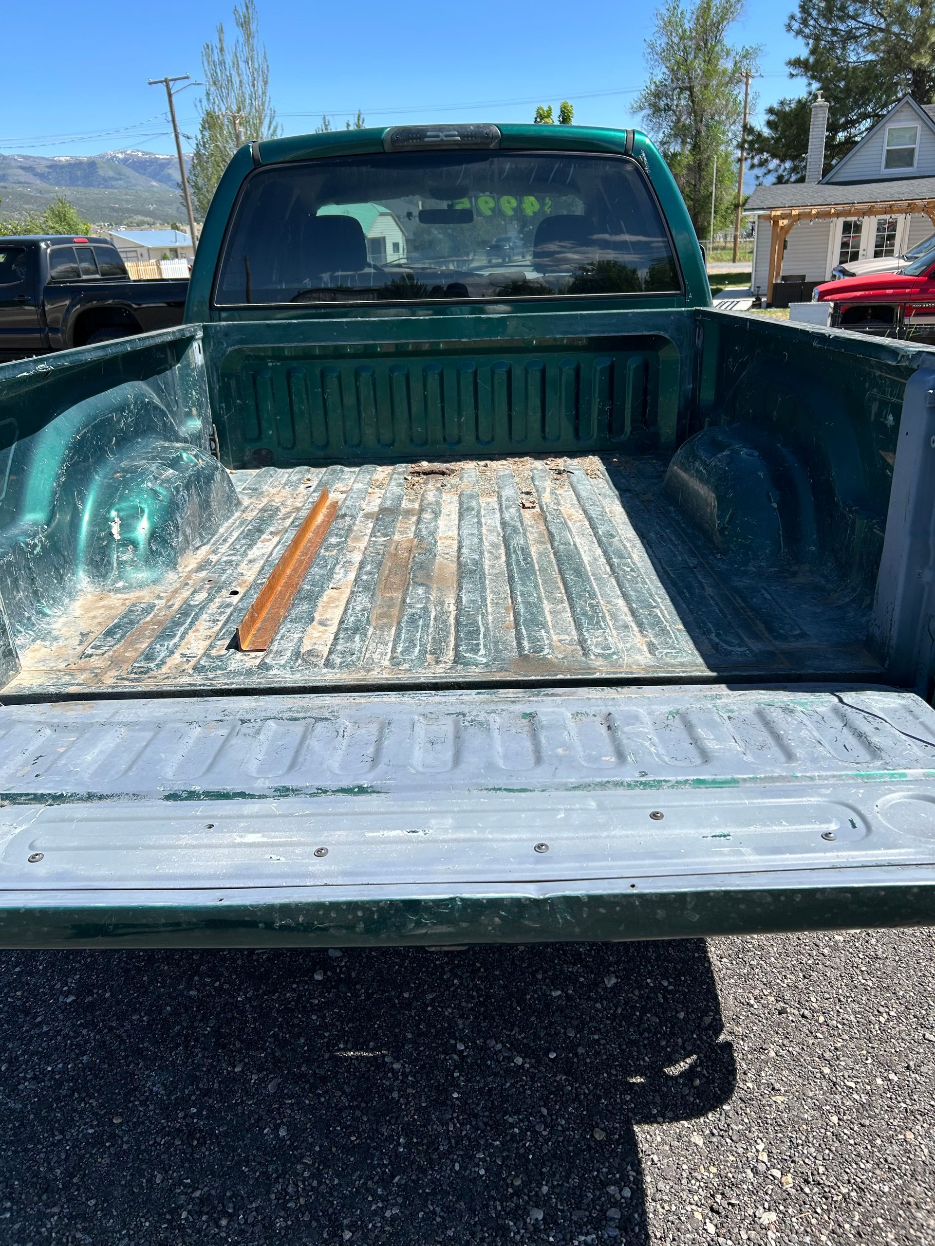 Empty pickup truck bed with a weathered metal liner, viewed from the tailgate in a sunny parking lot.