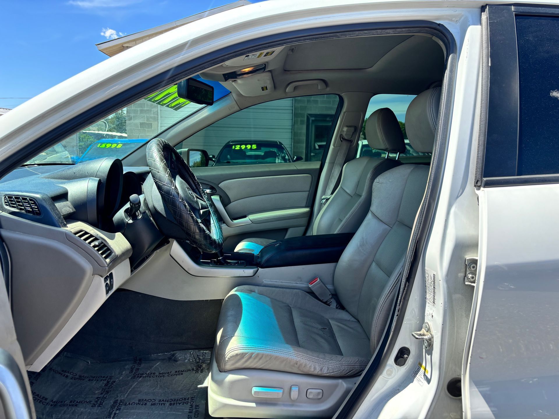 Open car door showing gray leather front seats and steering wheel inside a silver vehicle.