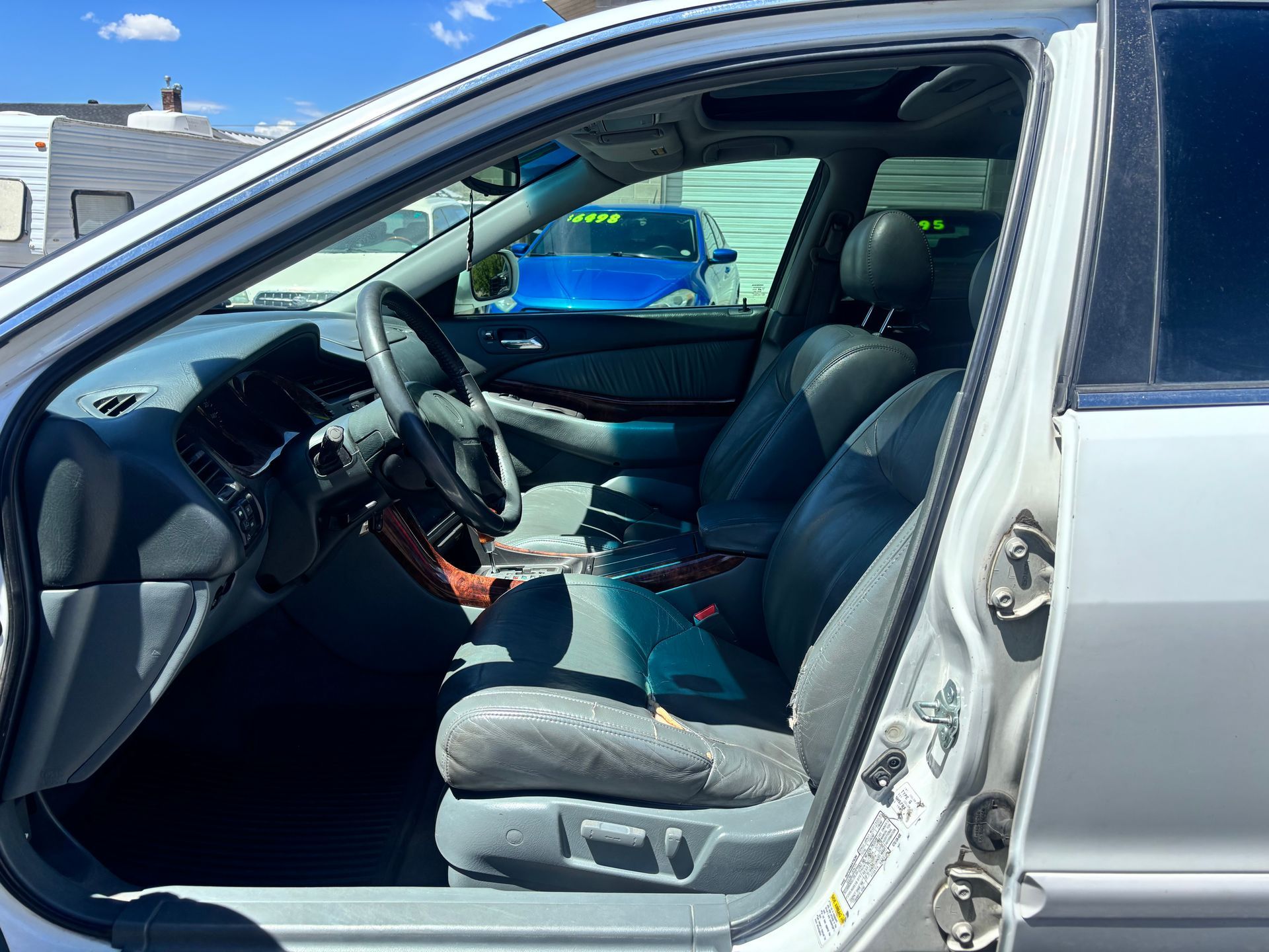Car interior with open driver’s door, black leather seats, and steering wheel in a silver vehicle
