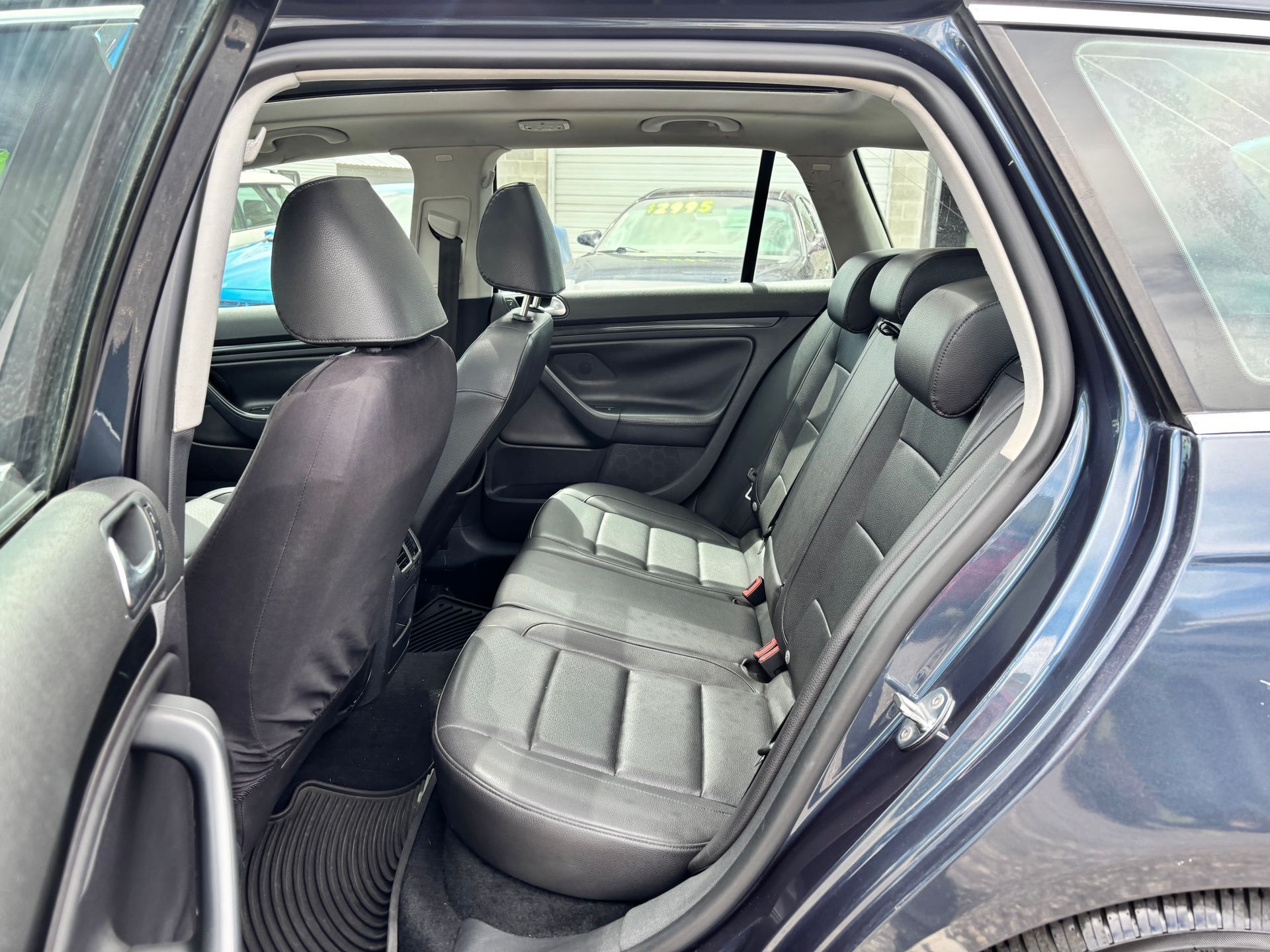 Car interior with rear seats and open door, showing dark upholstery and a view through the cabin.