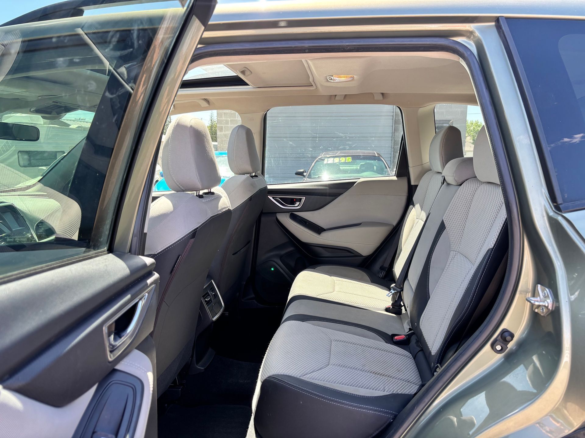 Open car rear door showing beige and black rear seats with folded seatback and sunlight inside
