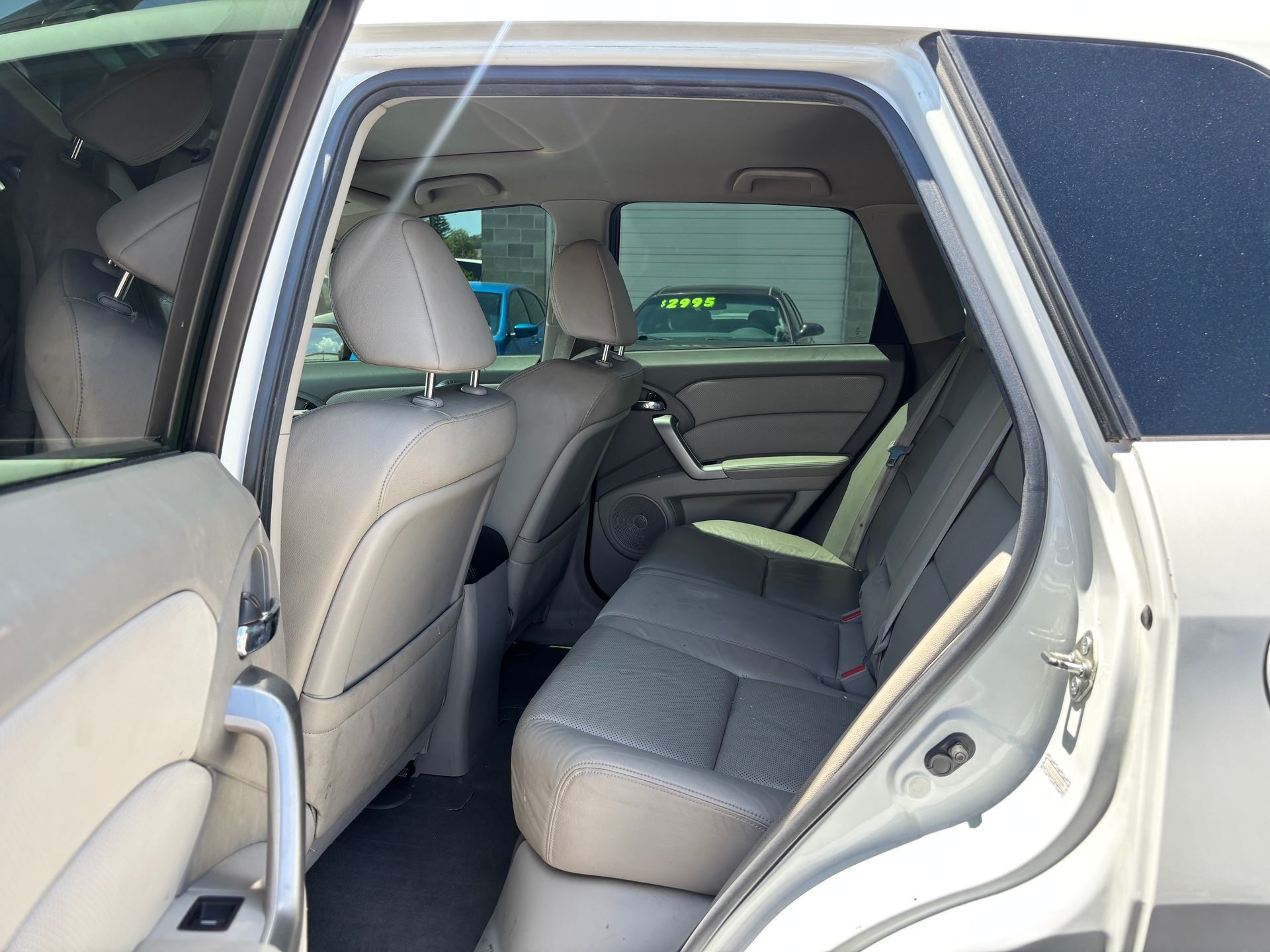 Open rear door of a beige car, showing the gray back seat and interior.