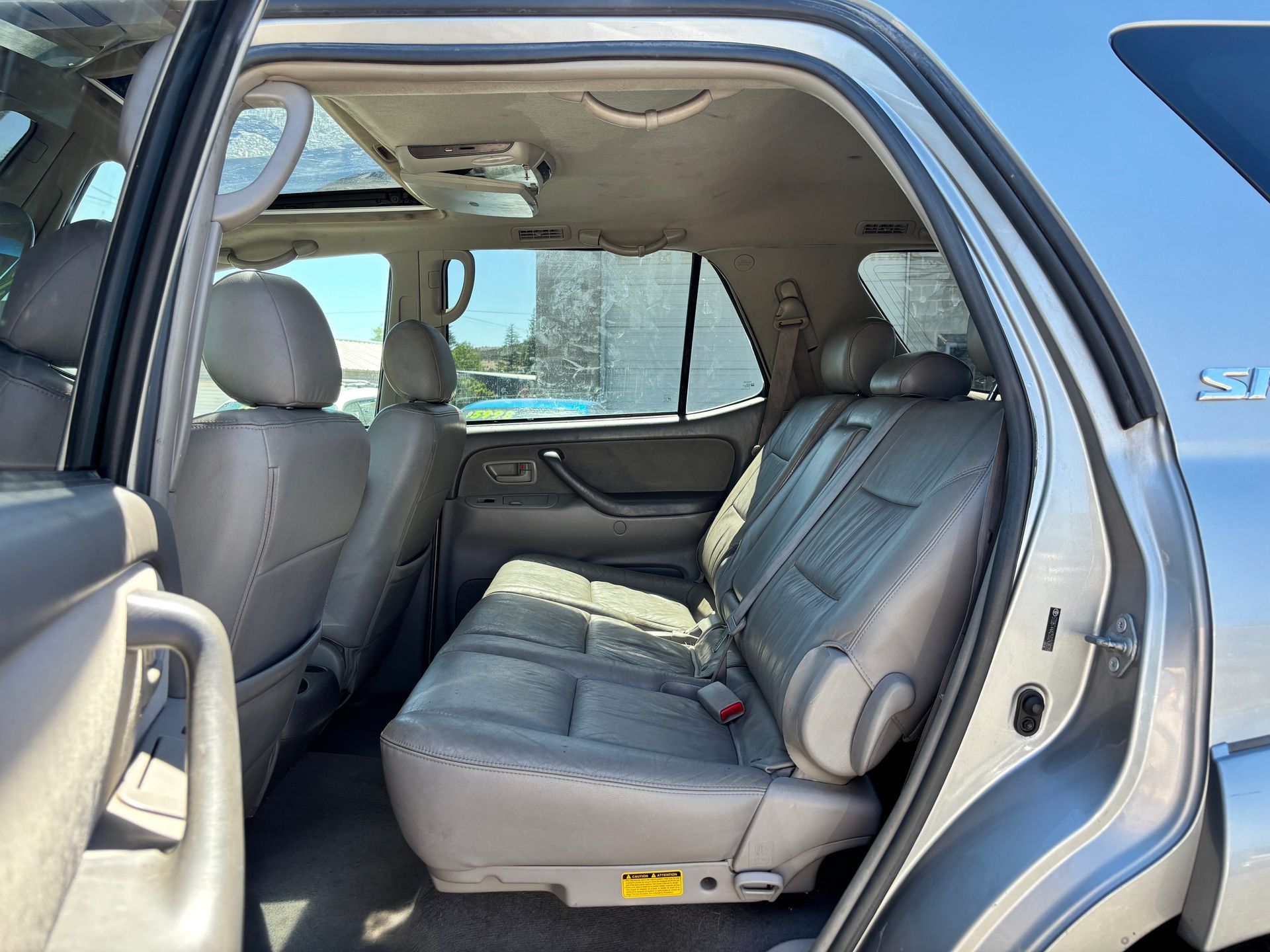 Open car door showing gray leather rear seat interior with headrests and seatbelt