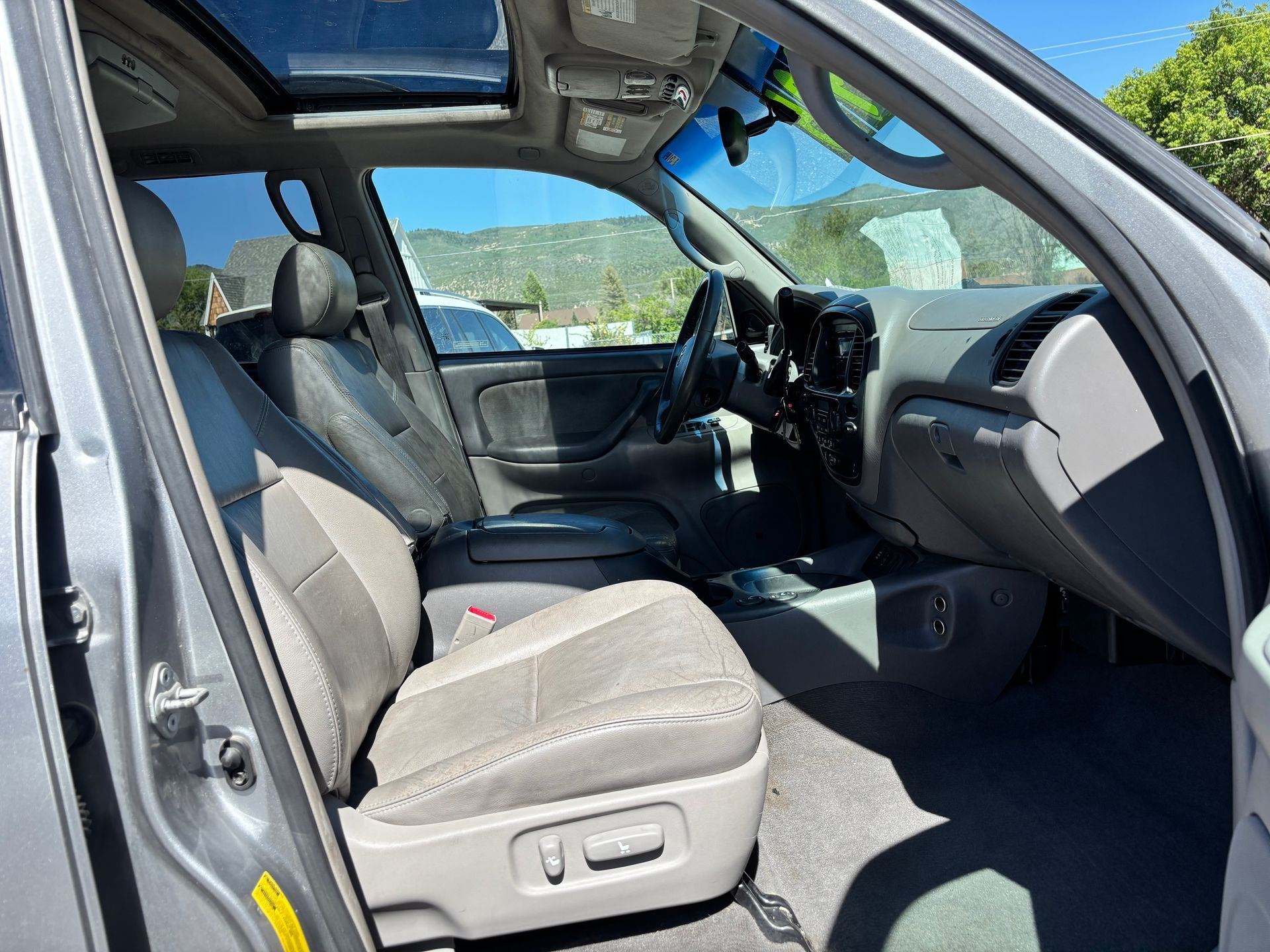 Open car interior with beige seats, dashboard, and sunroof, viewed from the driver’s side.