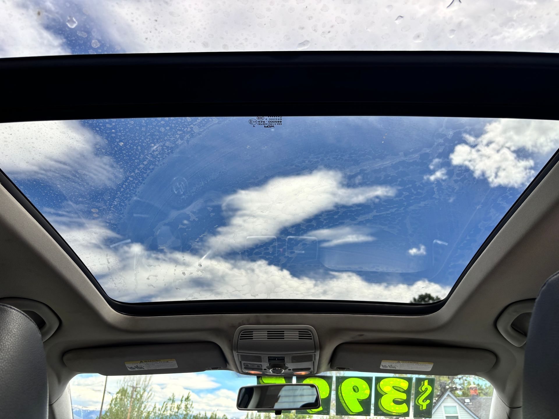 Car interior with sunroof showing blue sky and clouds above, dashboard visible below