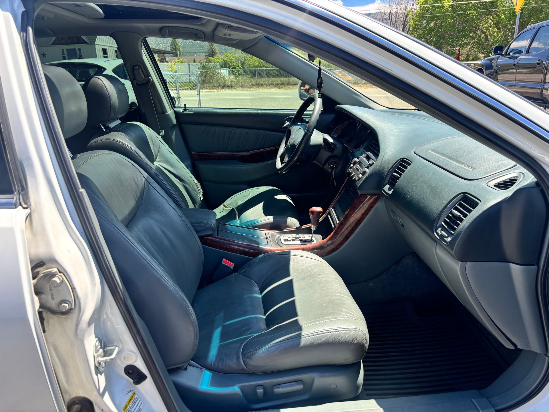 Car interior with open driver door, gray seats, and wood-trimmed dashboard in daylight
