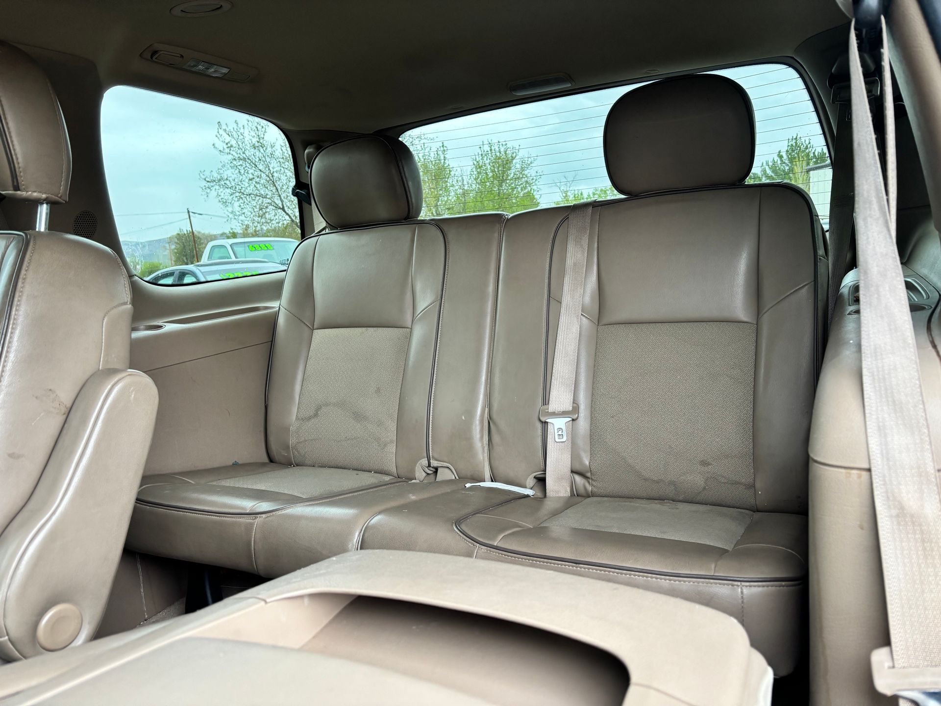 Tan leather minivan back seat with headrests and folded center armrest, viewed from inside.