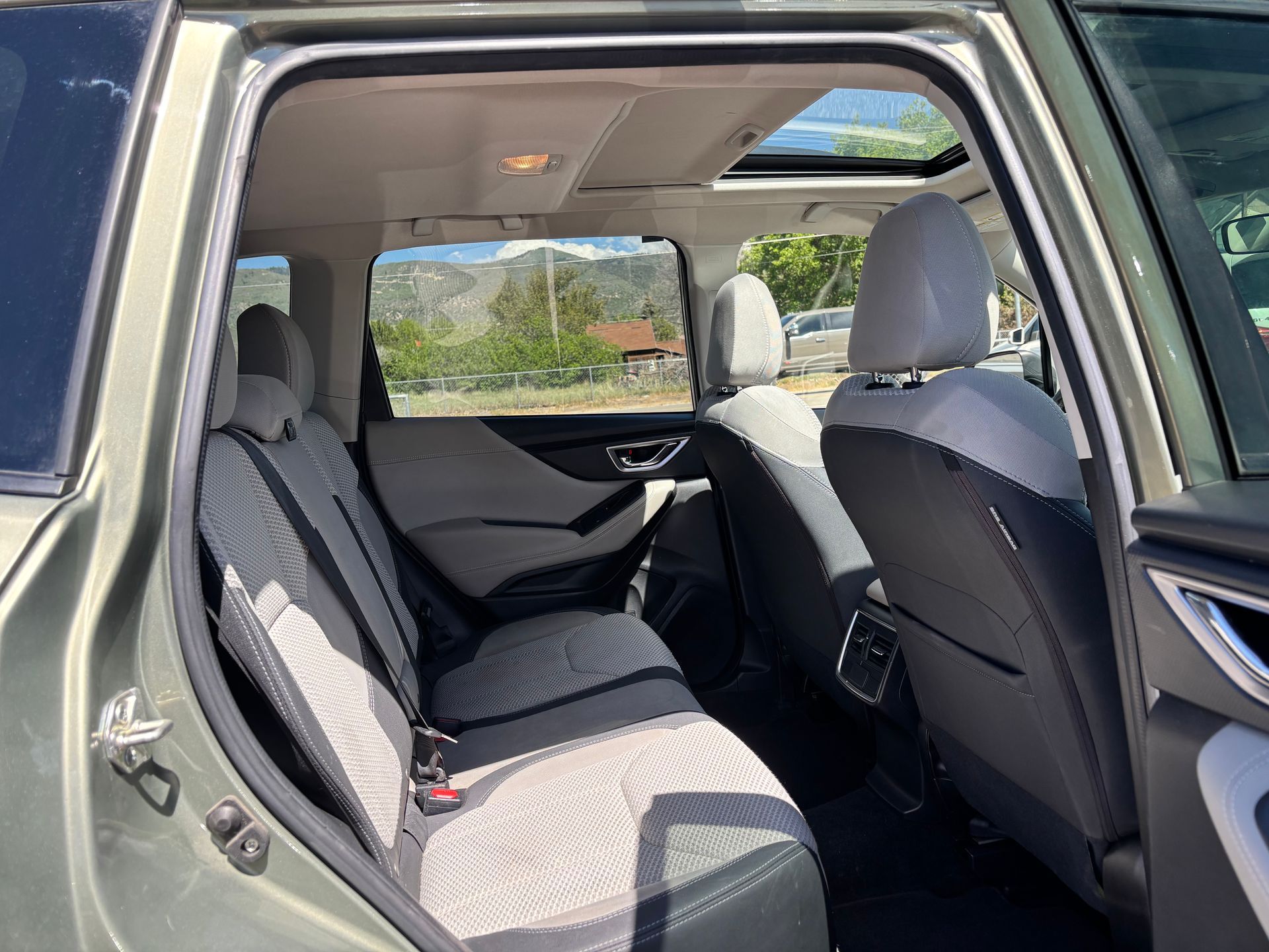 Car interior with rear passenger door open, showing gray cloth seats and a view through the windows.