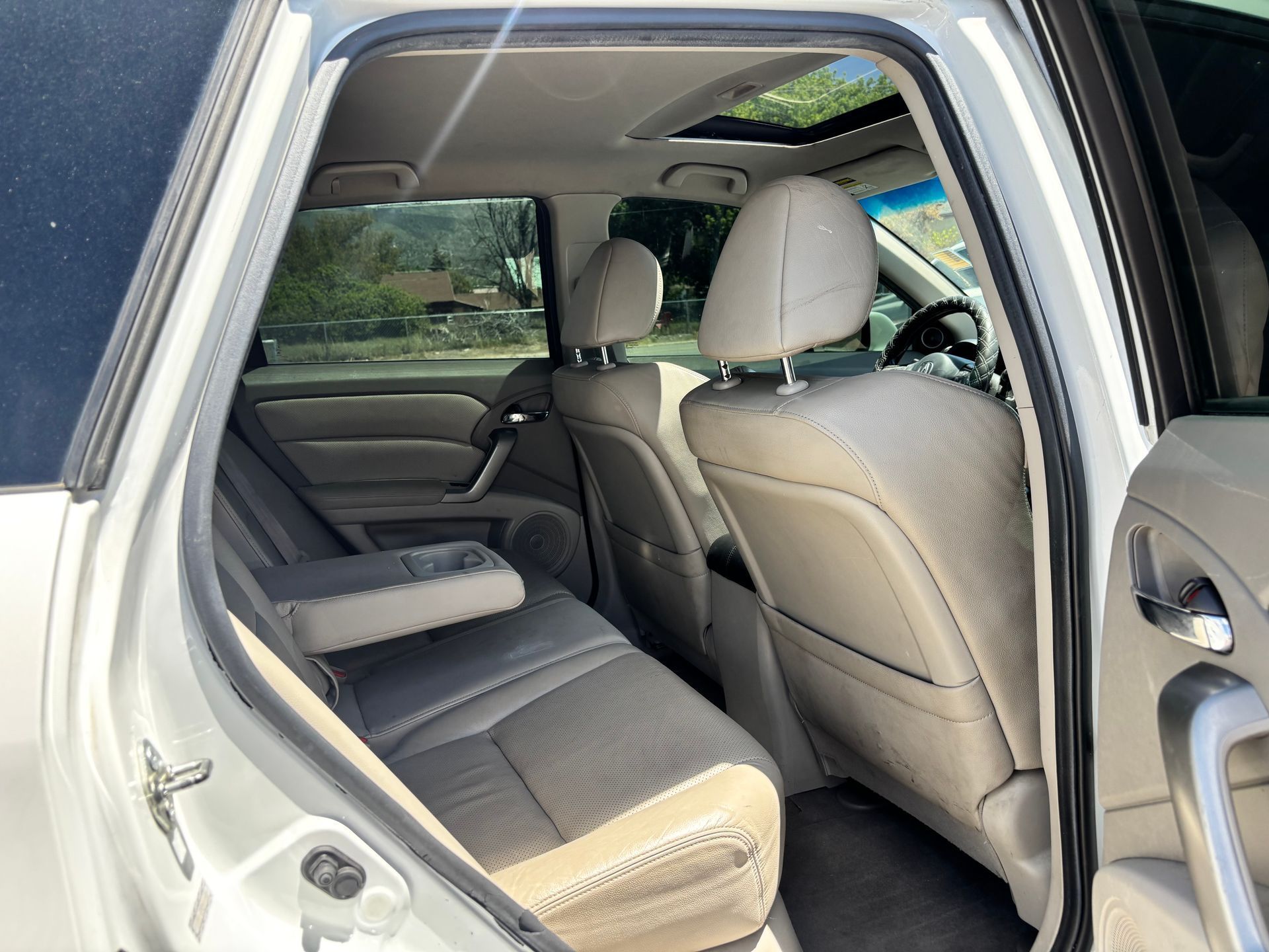 Car interior with rear seat and open door, showing beige upholstery and headrests.