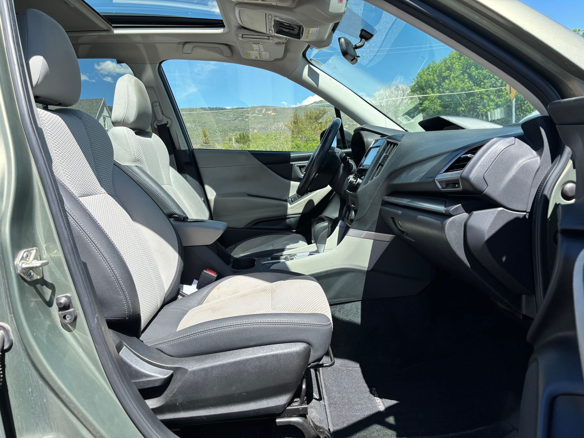 Open car interior with gray seats and dashboard, viewed from the driver’s side with the door open.