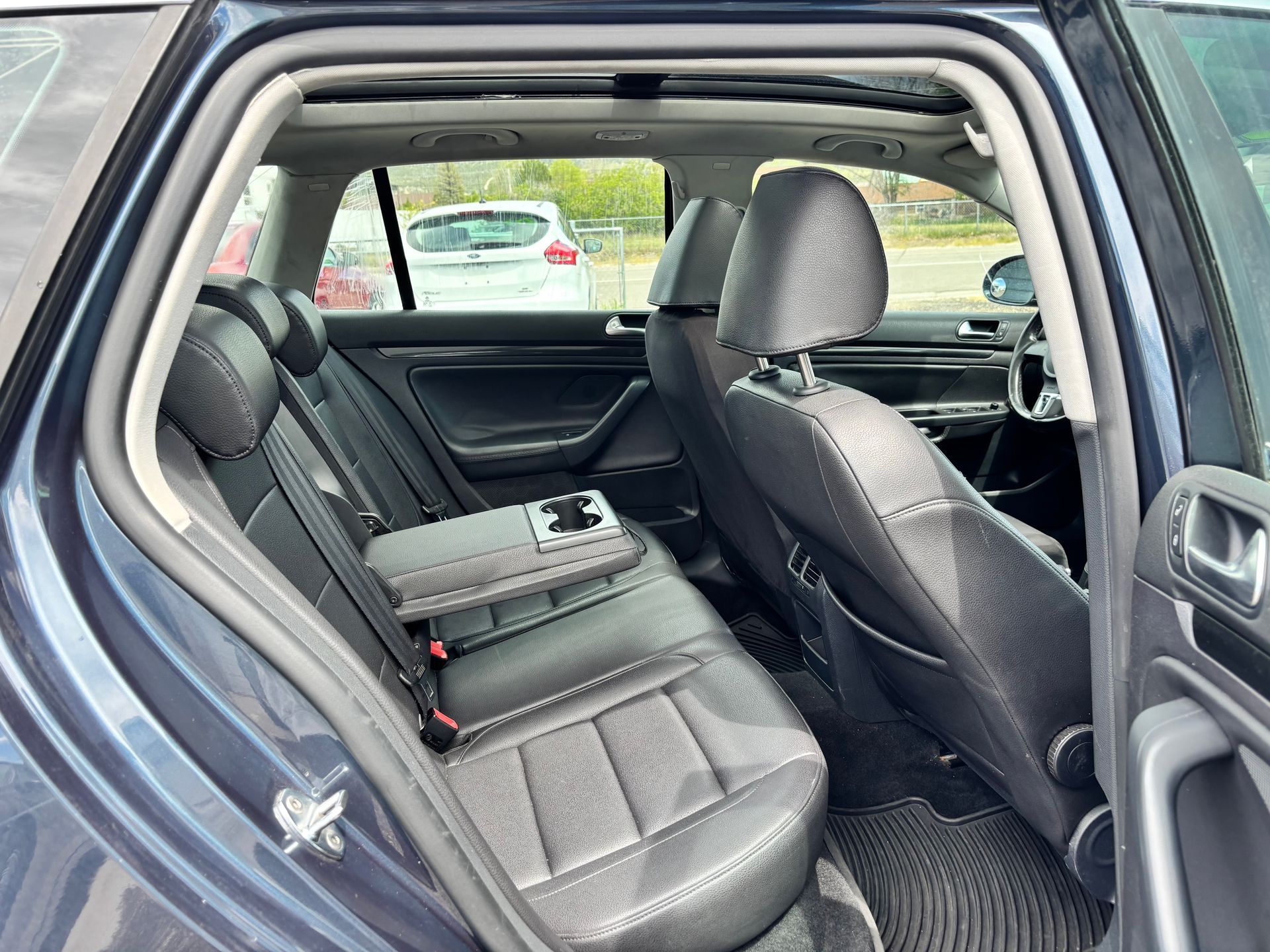 Open car door showing the rear seats of a blue vehicle, with a cushion on the left seat.
