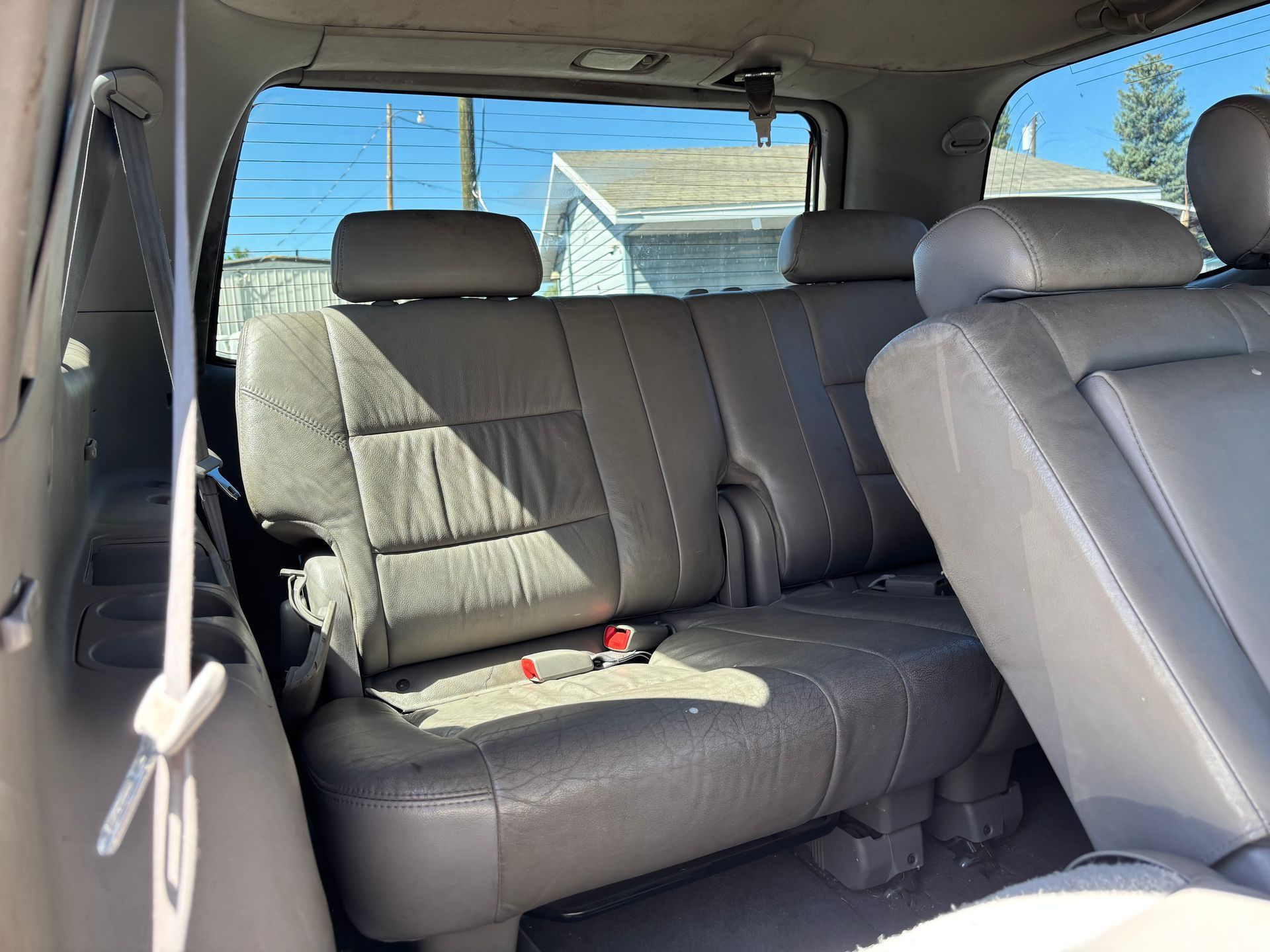 Back seat of a car with gray leather seats and a seatbelt hanging by the window.