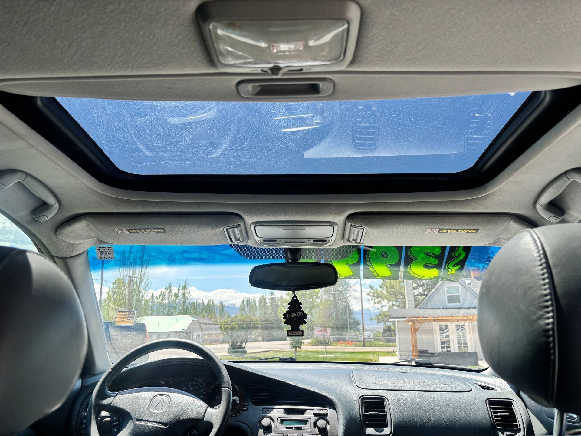 Inside a car, view of a dashboard, steering wheel, and sunroof under a blue sky.