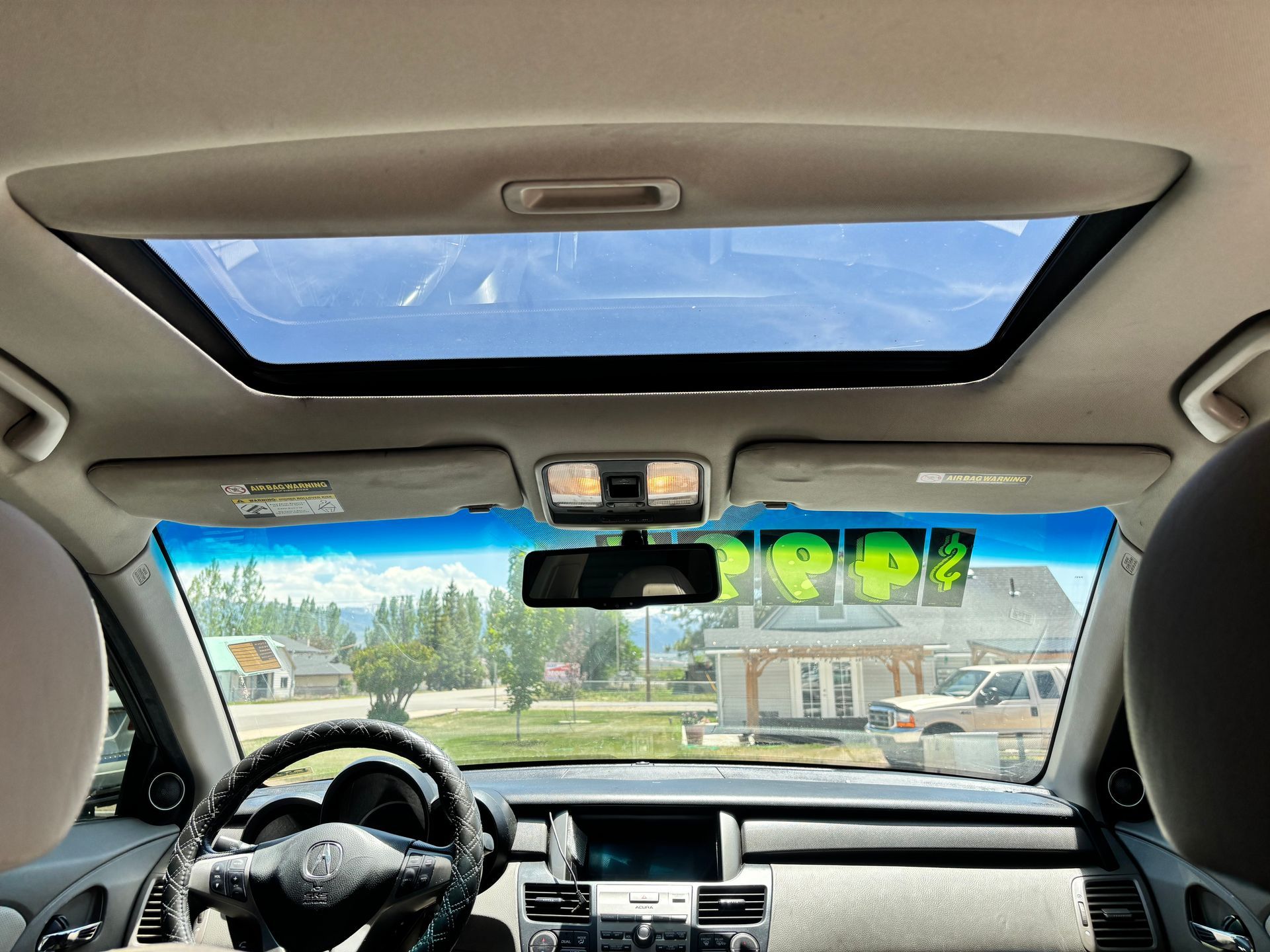 View from inside a car with a sunroof, dashboard, and a street scene ahead on a clear day.