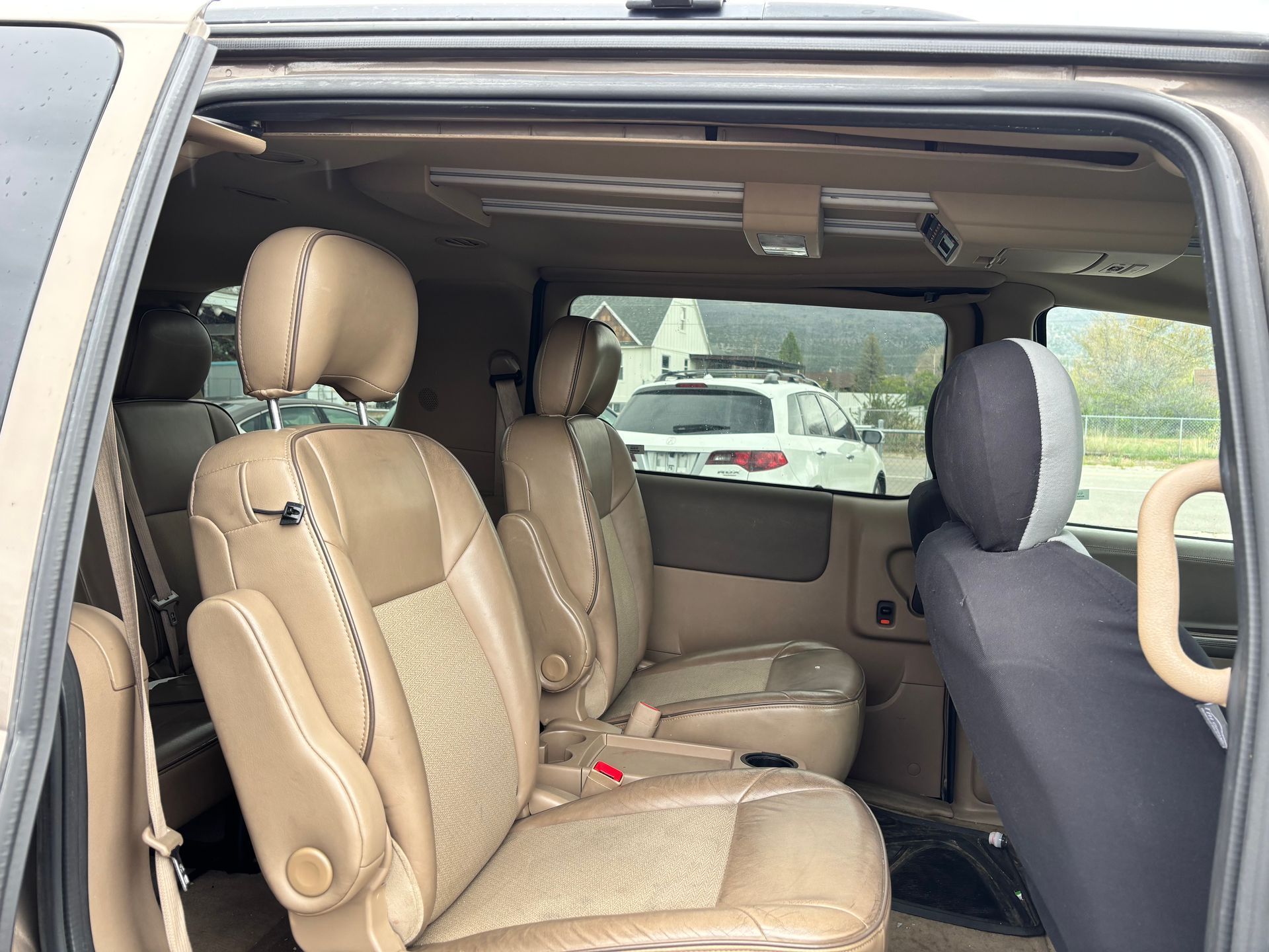 Car interior with tan leather seats and headrests, sliding side door open, showing the back row and windows.