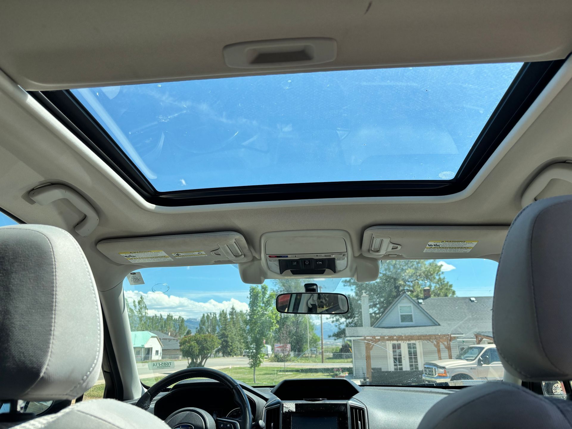 View from inside a car through an open sunroof, showing blue sky and a suburban neighborhood ahead.