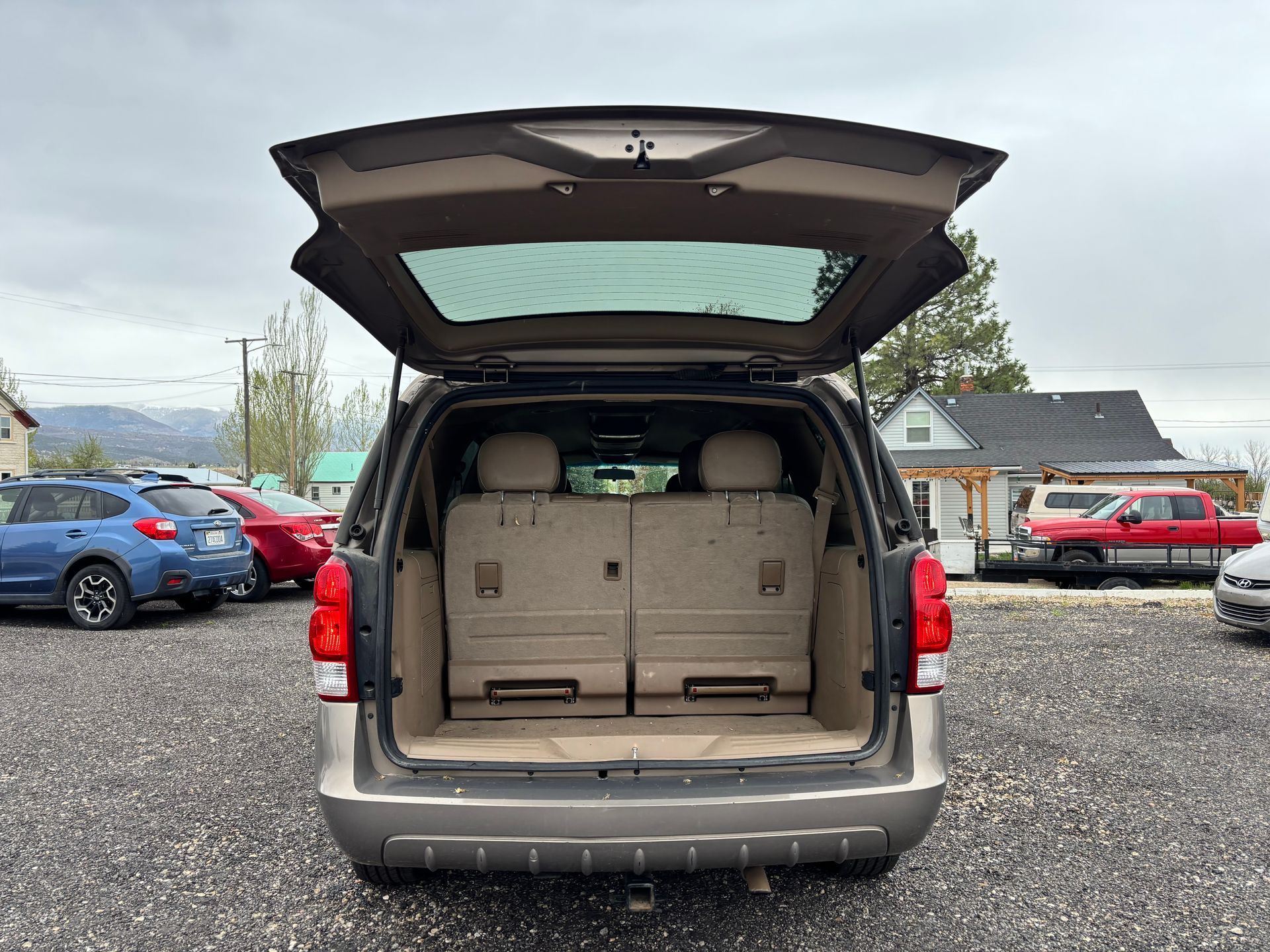 Open minivan trunk showing beige cargo area in a parking lot with cars and mountains beyond