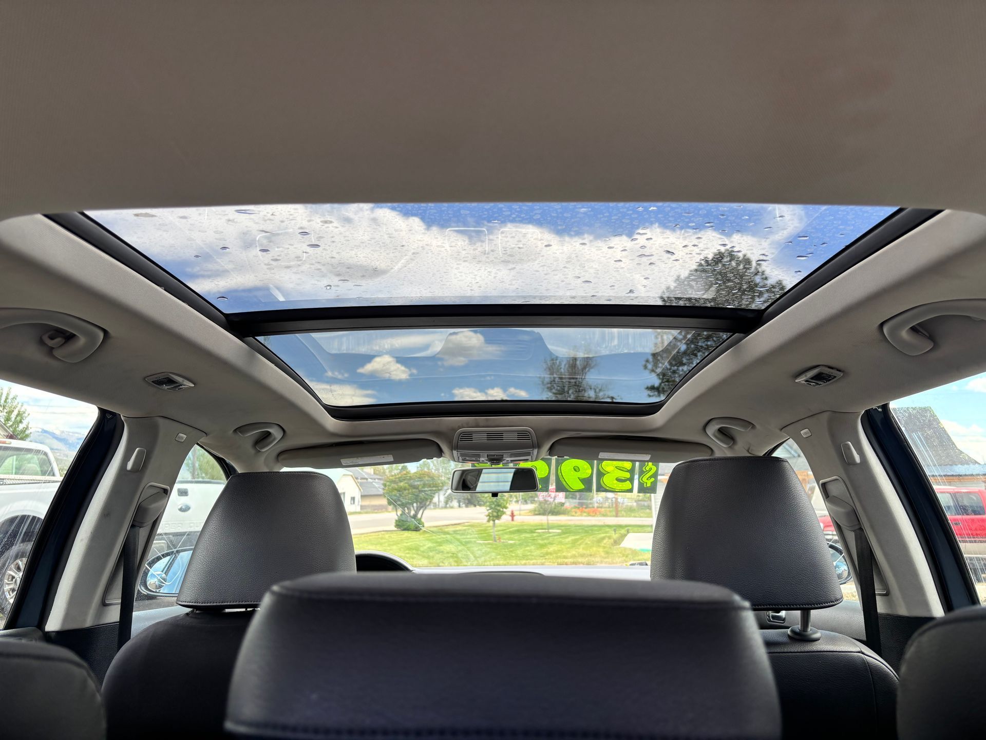 Car interior with panoramic sunroof, rear seat headrests, and a view of greenery through the windows