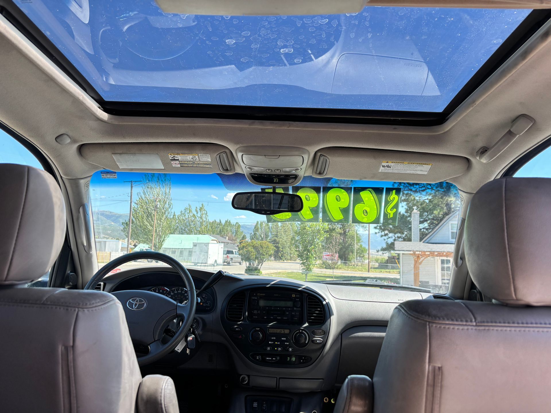 View from back seat of car with sunroof, dashboard, and bright green sale numbers on windshield
