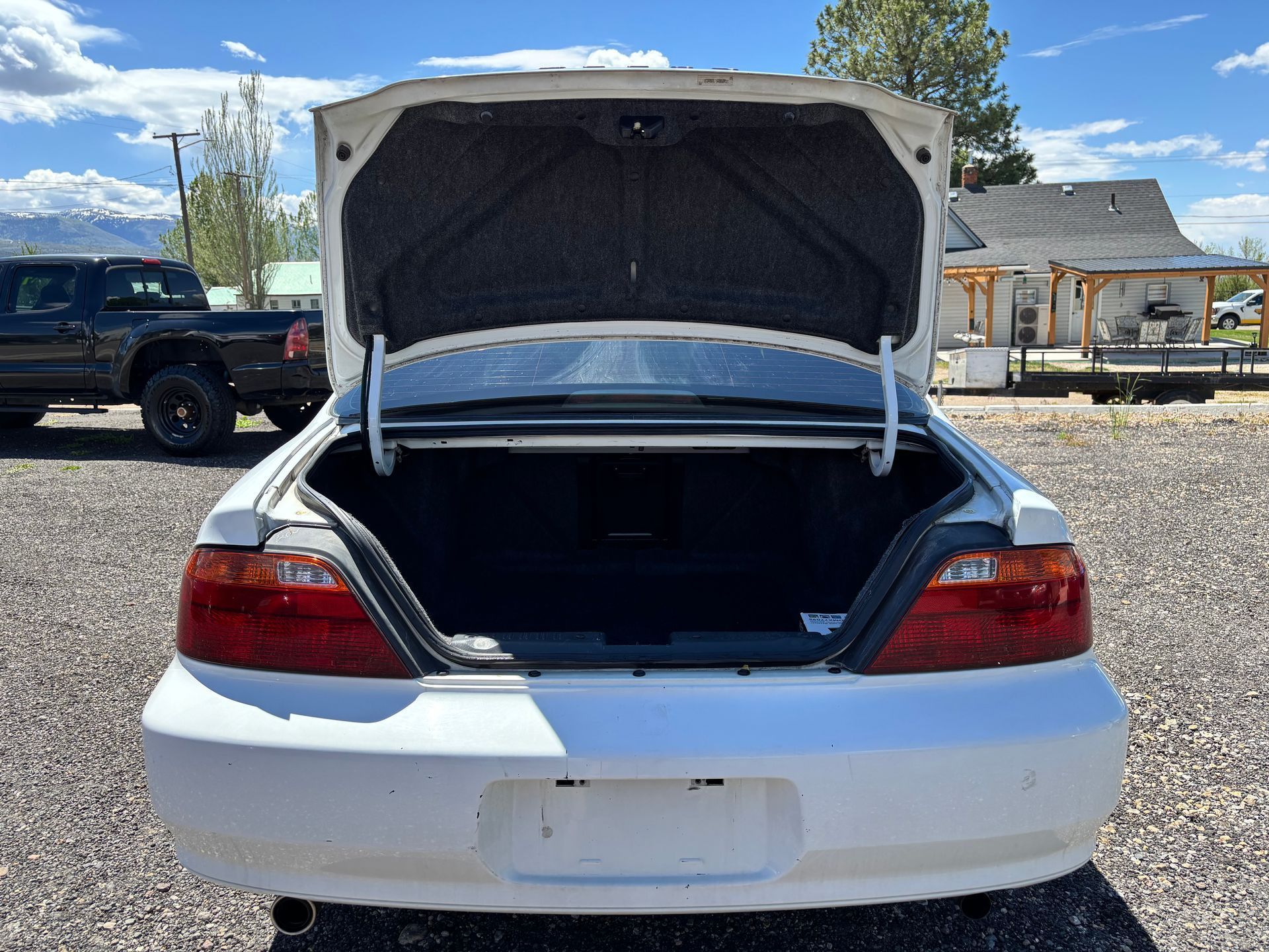 White car with open trunk in a parking lot, showing the empty trunk interior.