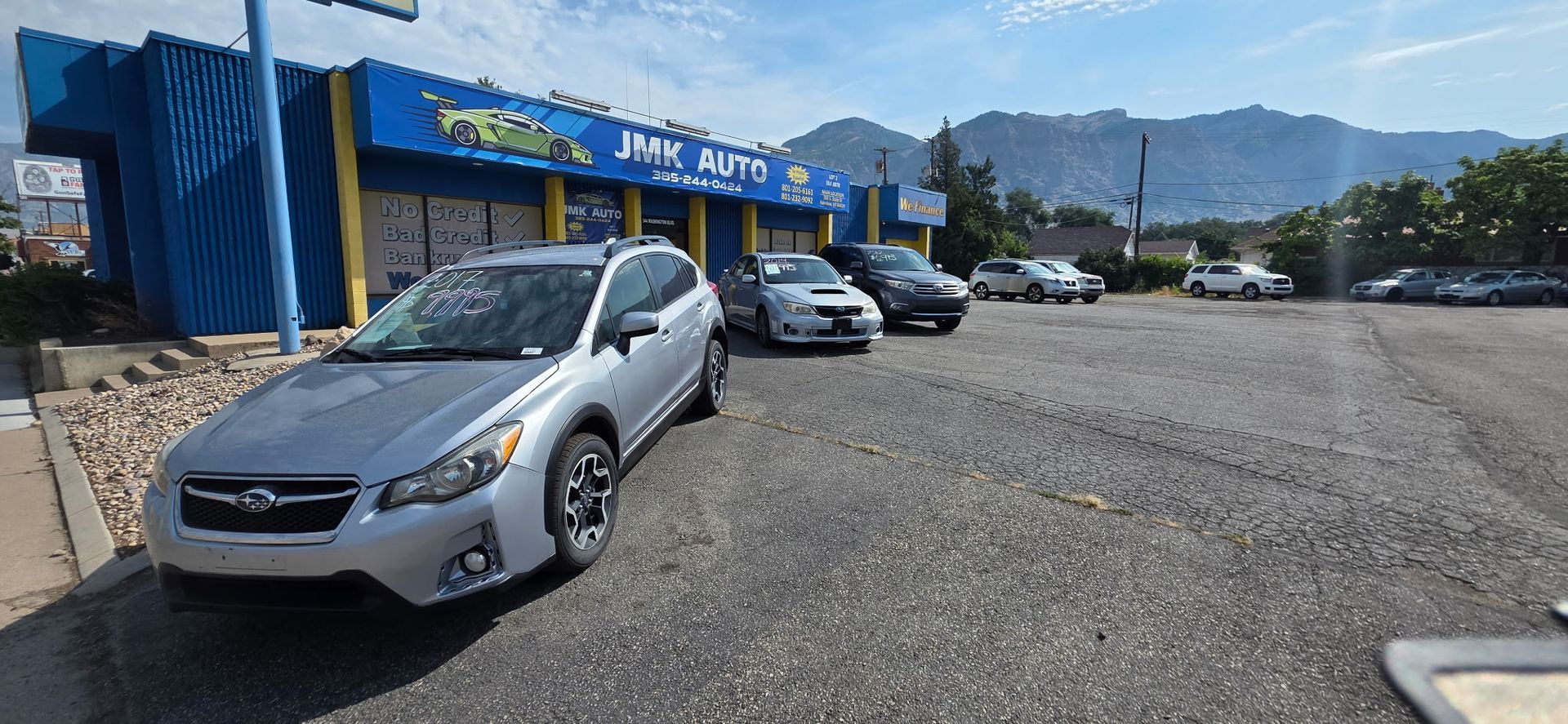 Silver car parked outside JMK Auto with mountains in the background