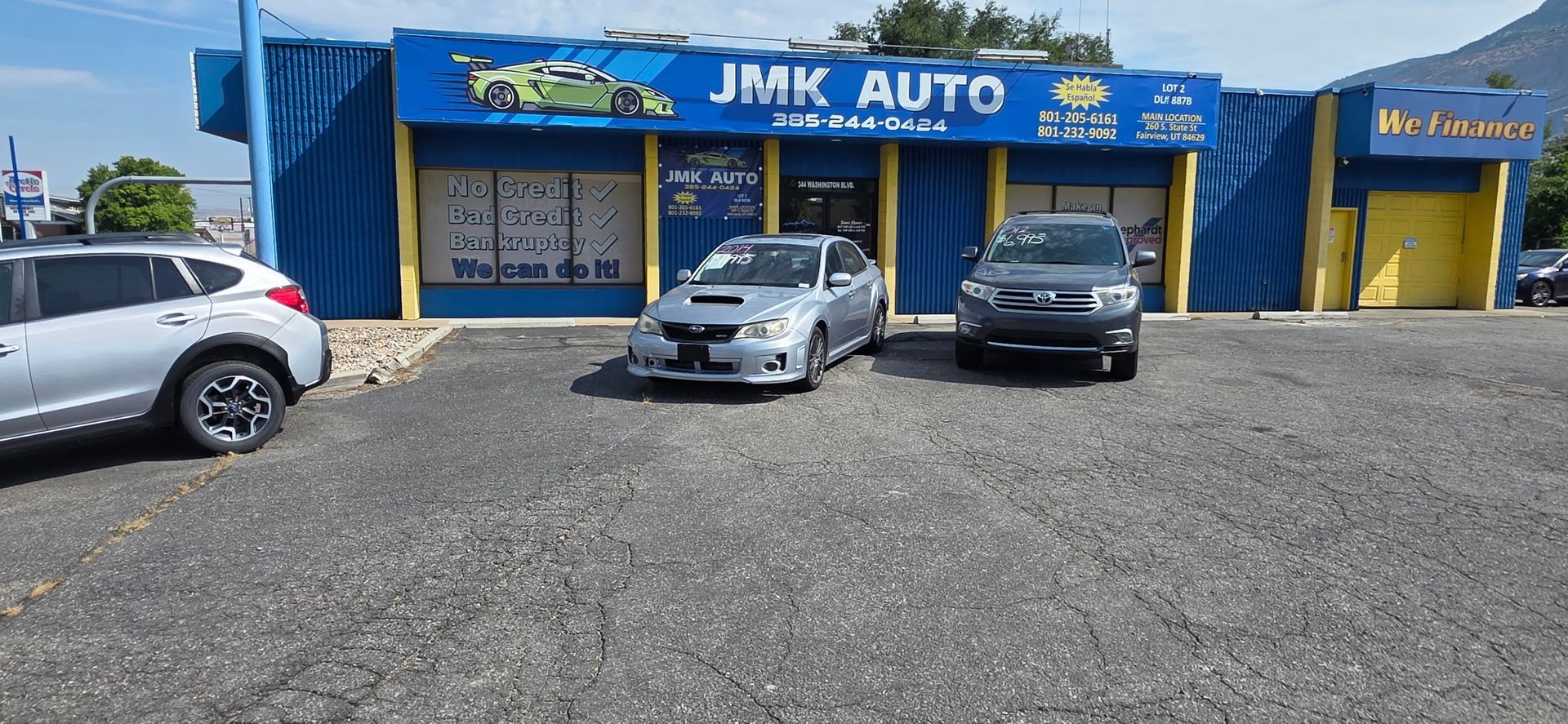 JMK Auto storefront with three parked cars and a gravel lot on a sunny day