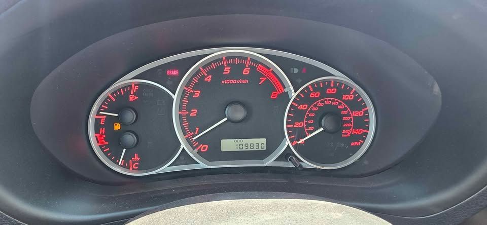 Car dashboard instrument cluster with red-lit speedometer, tachometer, and fuel gauges.
