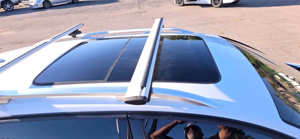 Silver car roof with tinted sunroof and roof rack bars parked on pavement