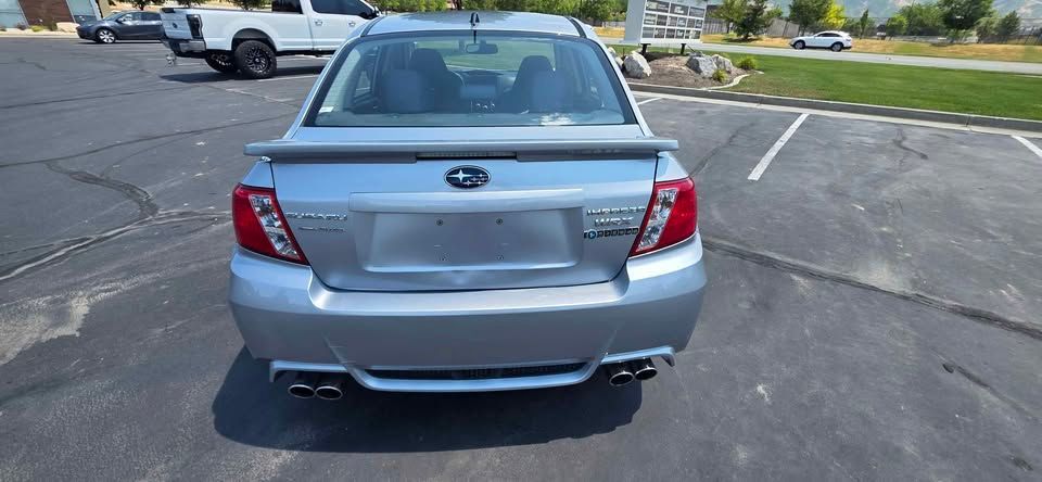 Rear view of a silver Subaru sedan parked in a lot, with damage on the rear bumper and trunk.