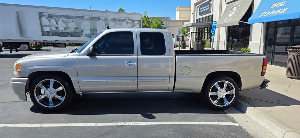 Silver pickup truck parked beside a sidewalk in front of a building with a blue awning.