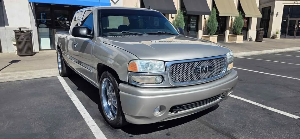 Silver GMC pickup truck parked in a lot outside storefronts on a sunny day